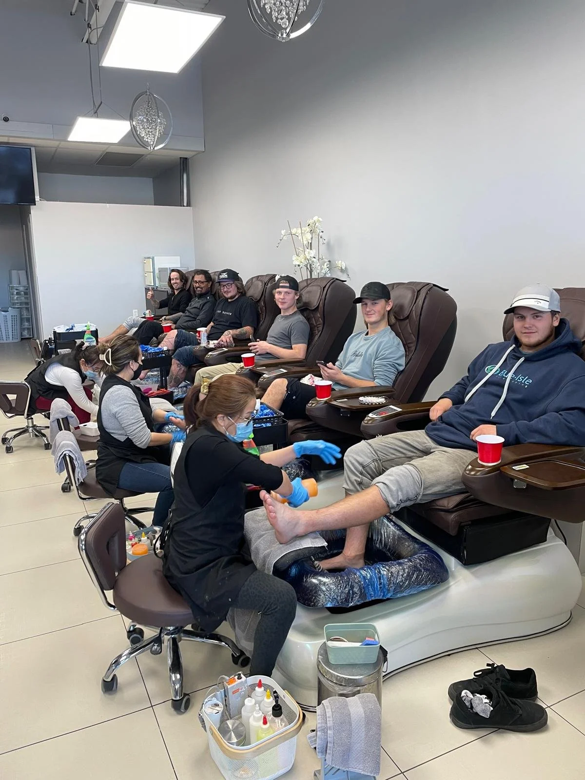 People receiving foot massages at a nail salon, with technicians attending to their feet, in a modern, well-lit establishment.