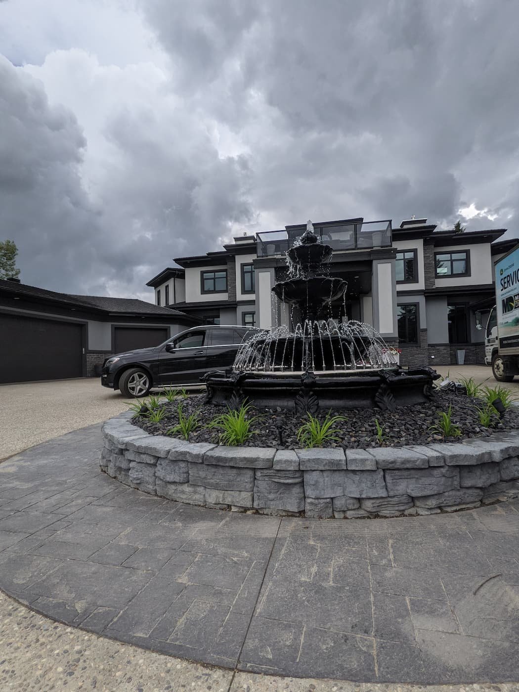 Large circular fountain in middle of a driveway surrounded by greens and landscaping rock