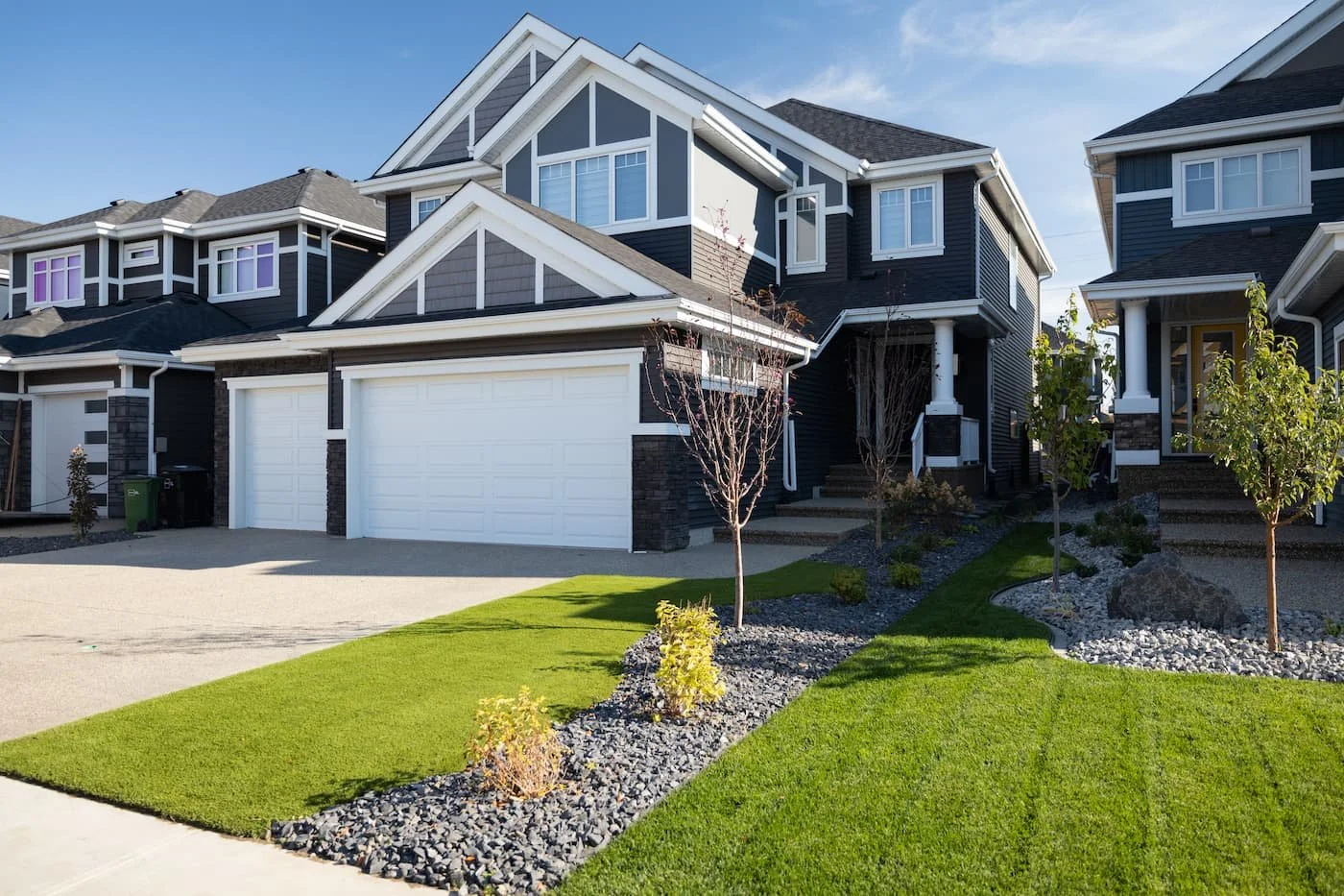 A front yard with artificial turf, landscape rock, shrubs and deciduous trees