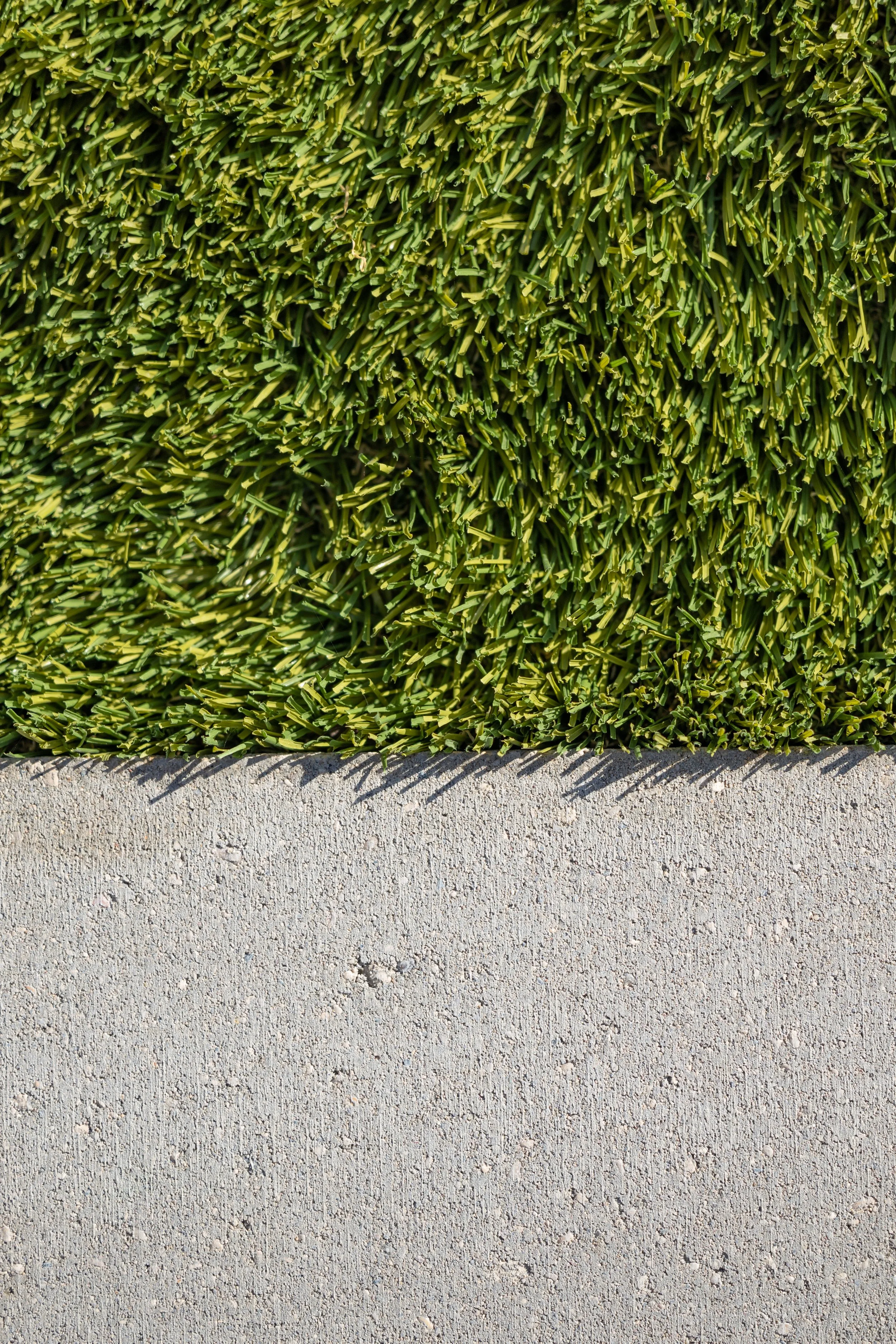 Close-up of a green artificial turf grass section next to a light gray concrete sidewalk.