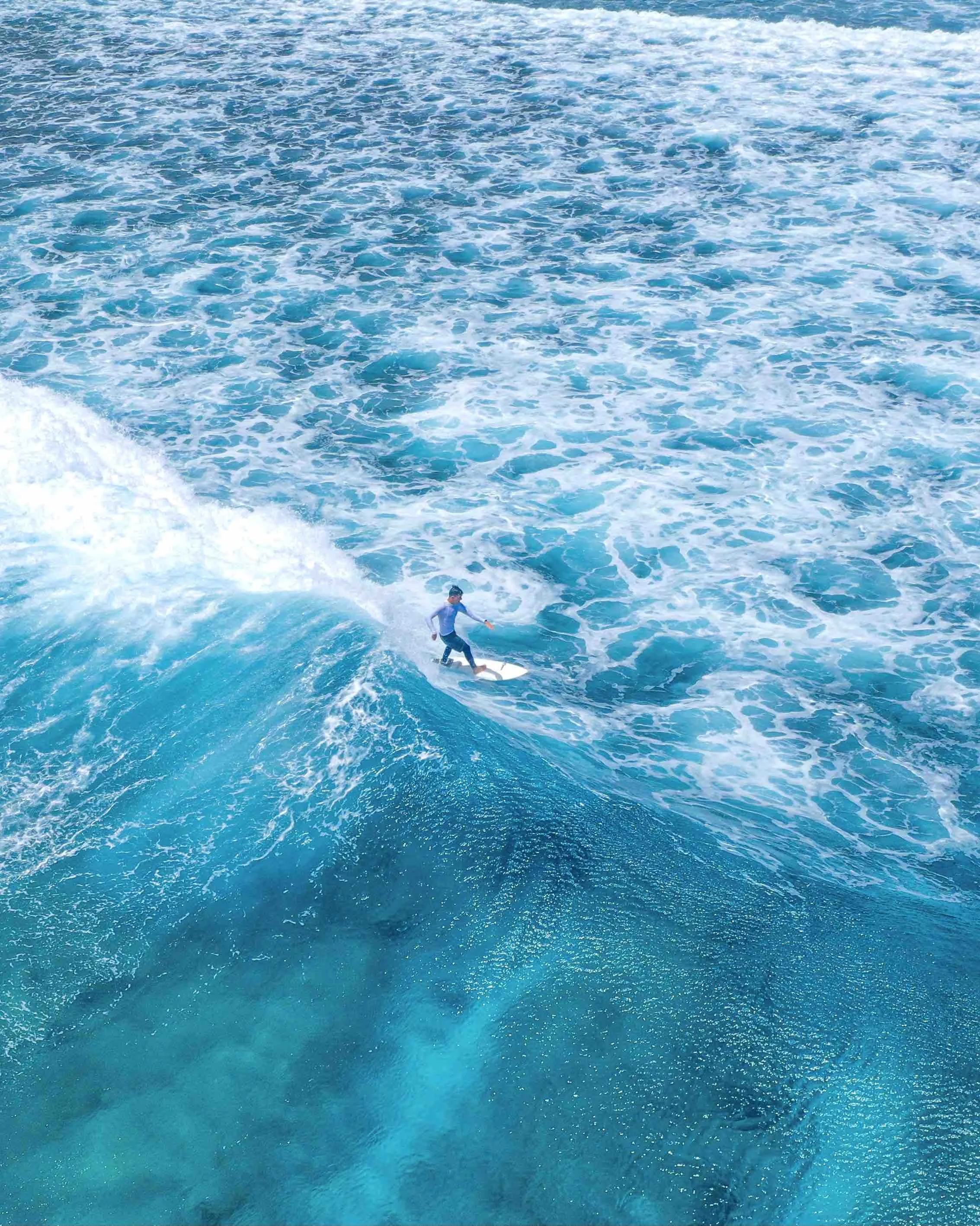 A person surfing on a blue ocean wave with white foam.