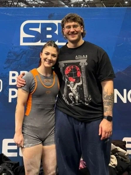 A young woman and a man standing together, smiling, at a sports event with an SBS logo in the background.