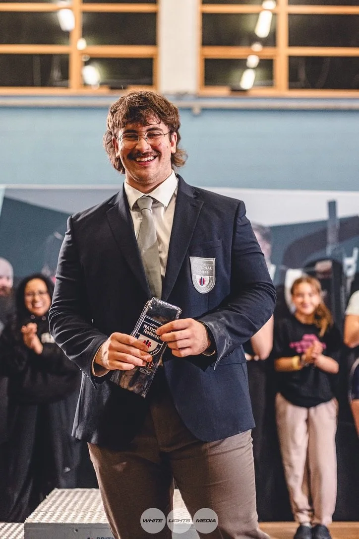 Man in suit holding an award at a reception, smiling, with people clapping in the background.