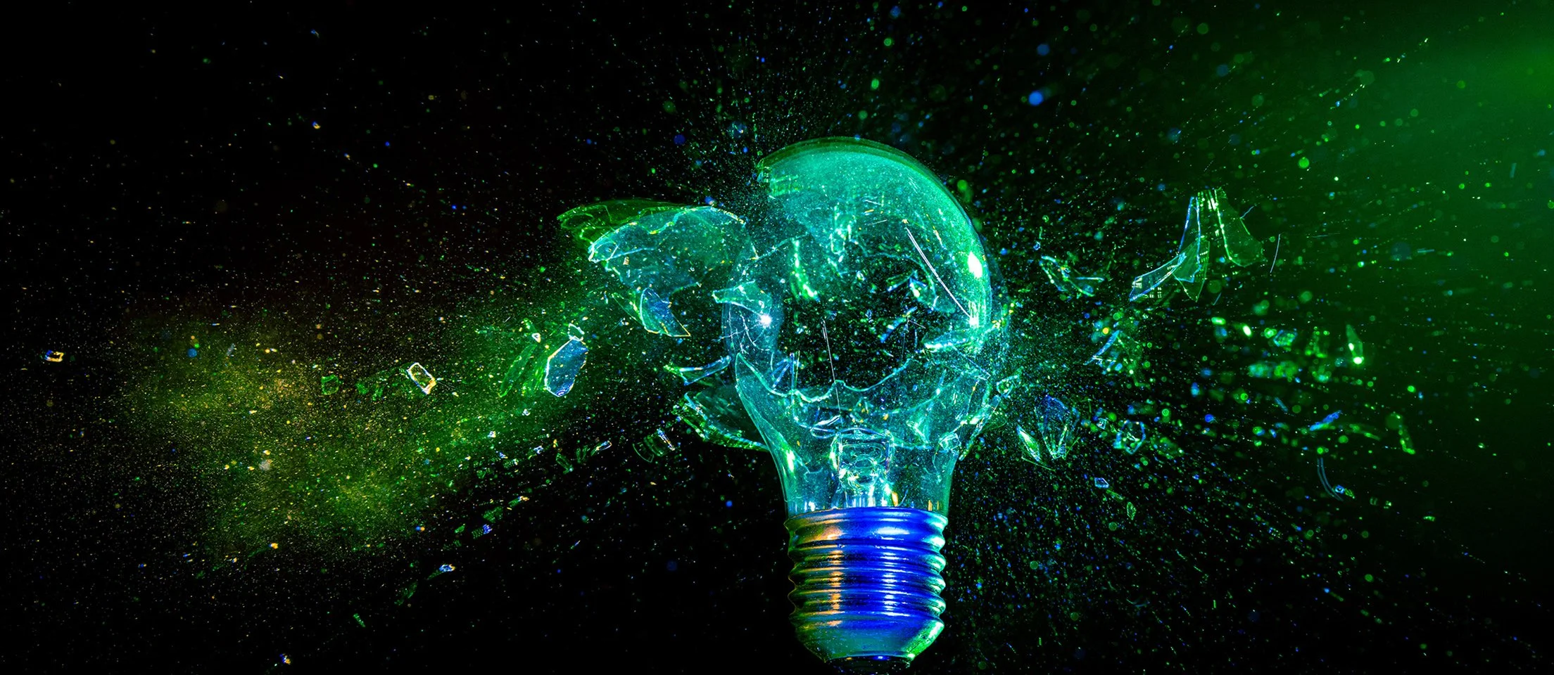 A shattered green glass light bulb with bright green and blue lights, exploding into small fragments against a dark background.