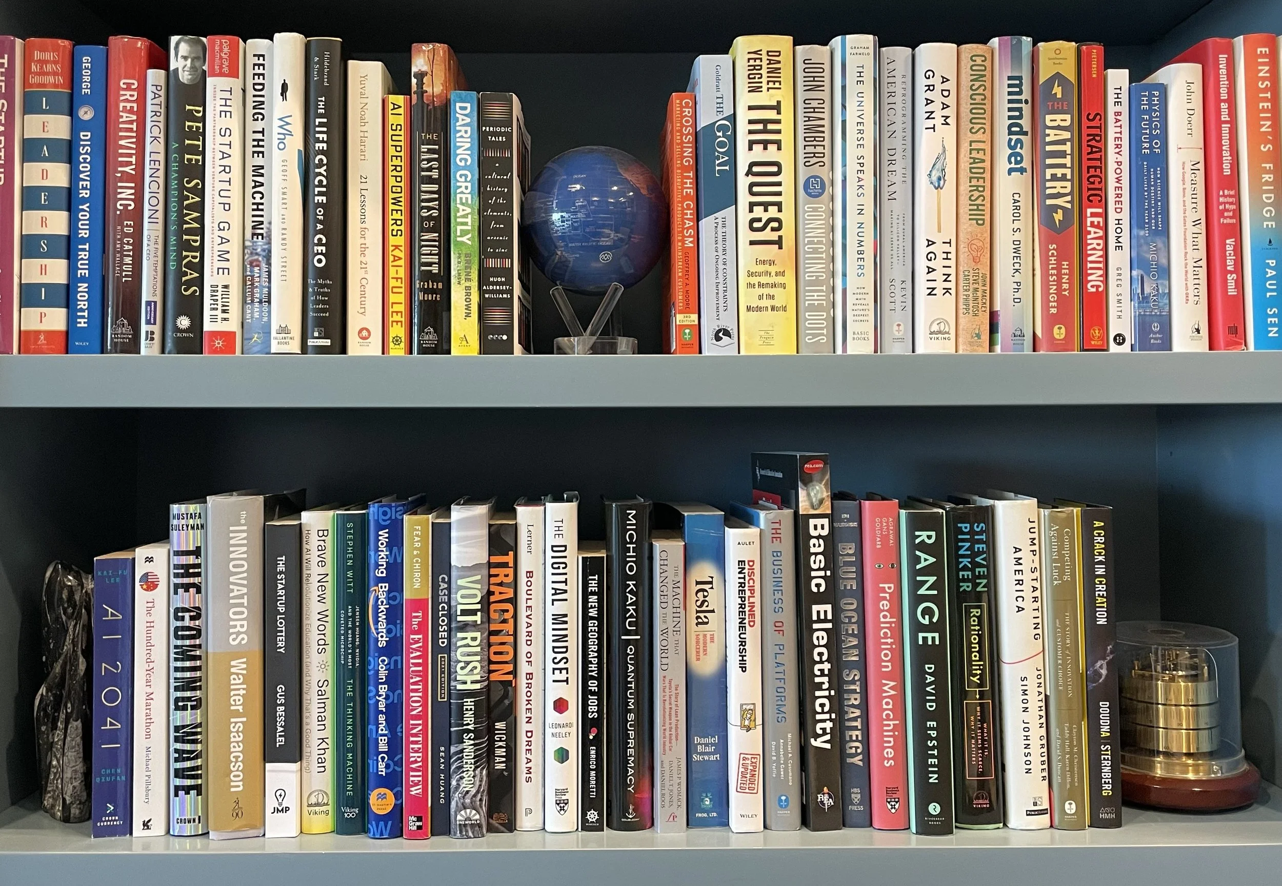 Bookshelf with two shelves filled with various books and a small globe in the middle of the top shelf.