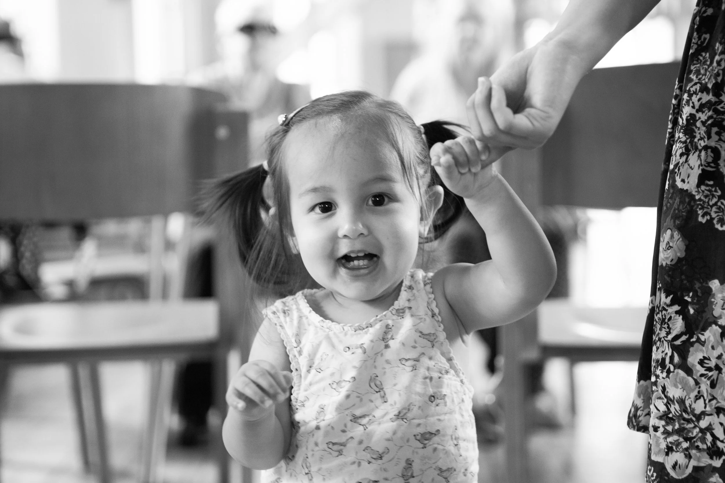 A young girl with pigtails smiling and holding an adult's hand.