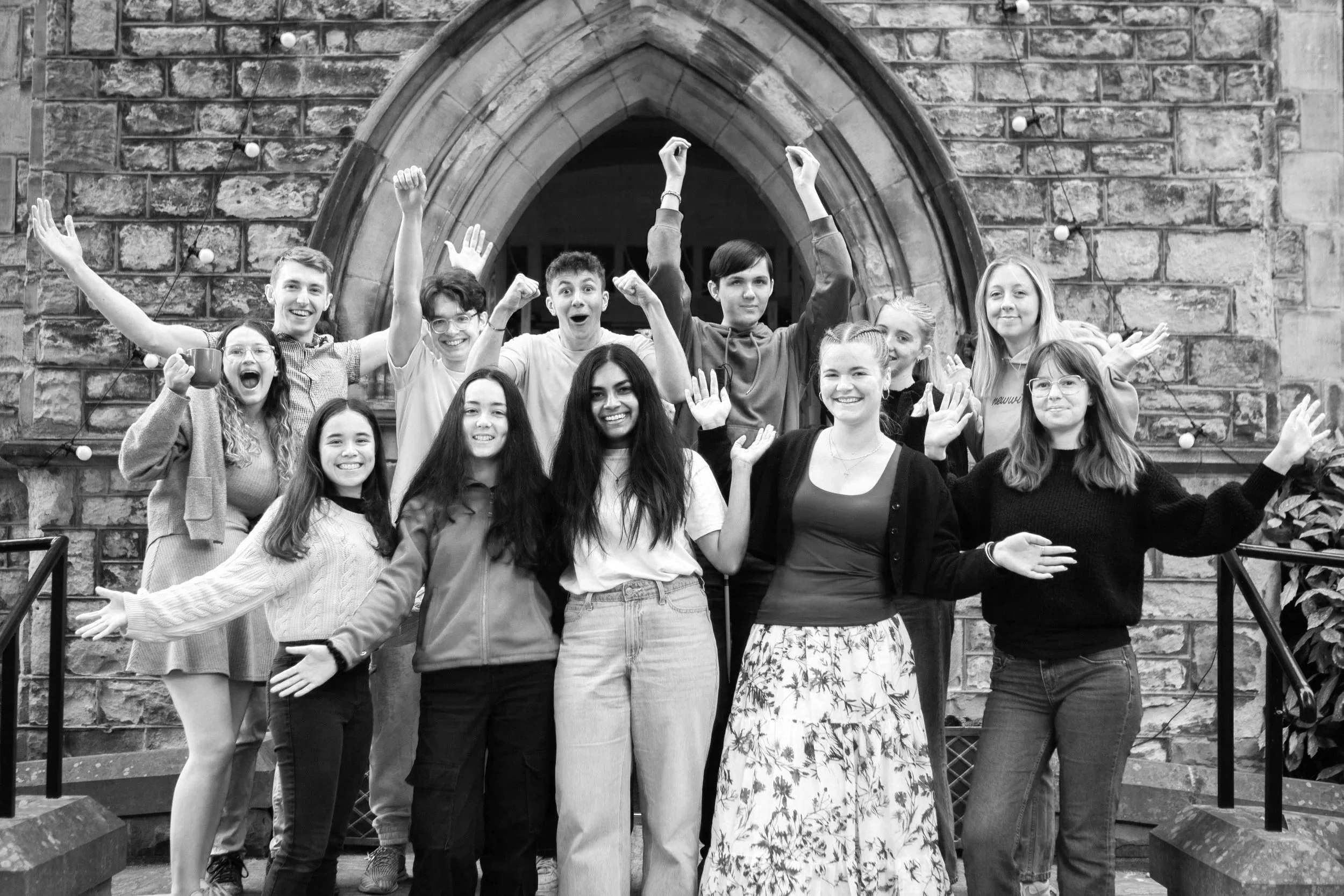 Group of teenagers and young adults celebrating outdoors in front of a stone archway