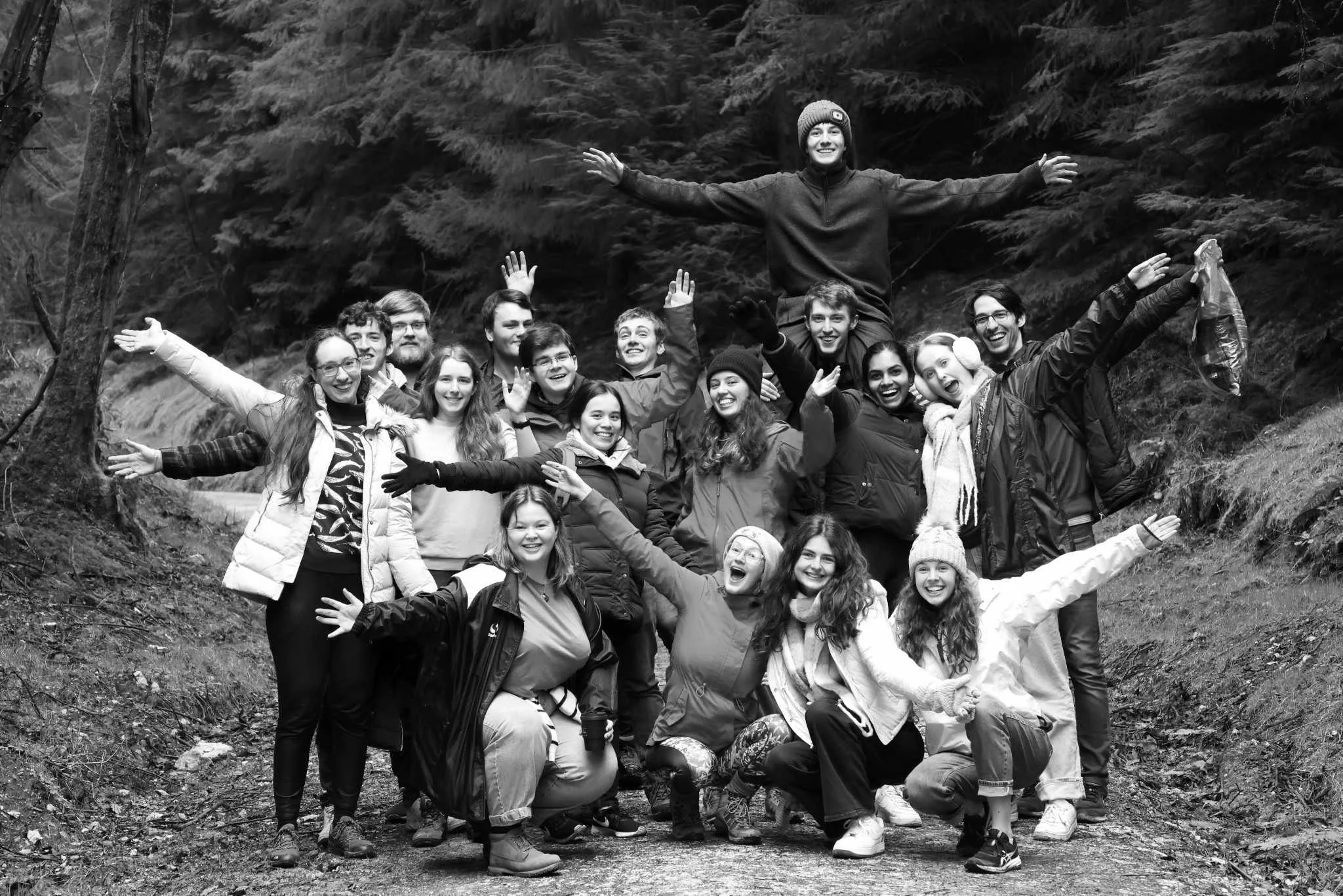 A group of people posing outdoors in a forest, some with their arms outstretched, smiling and celebrating together.