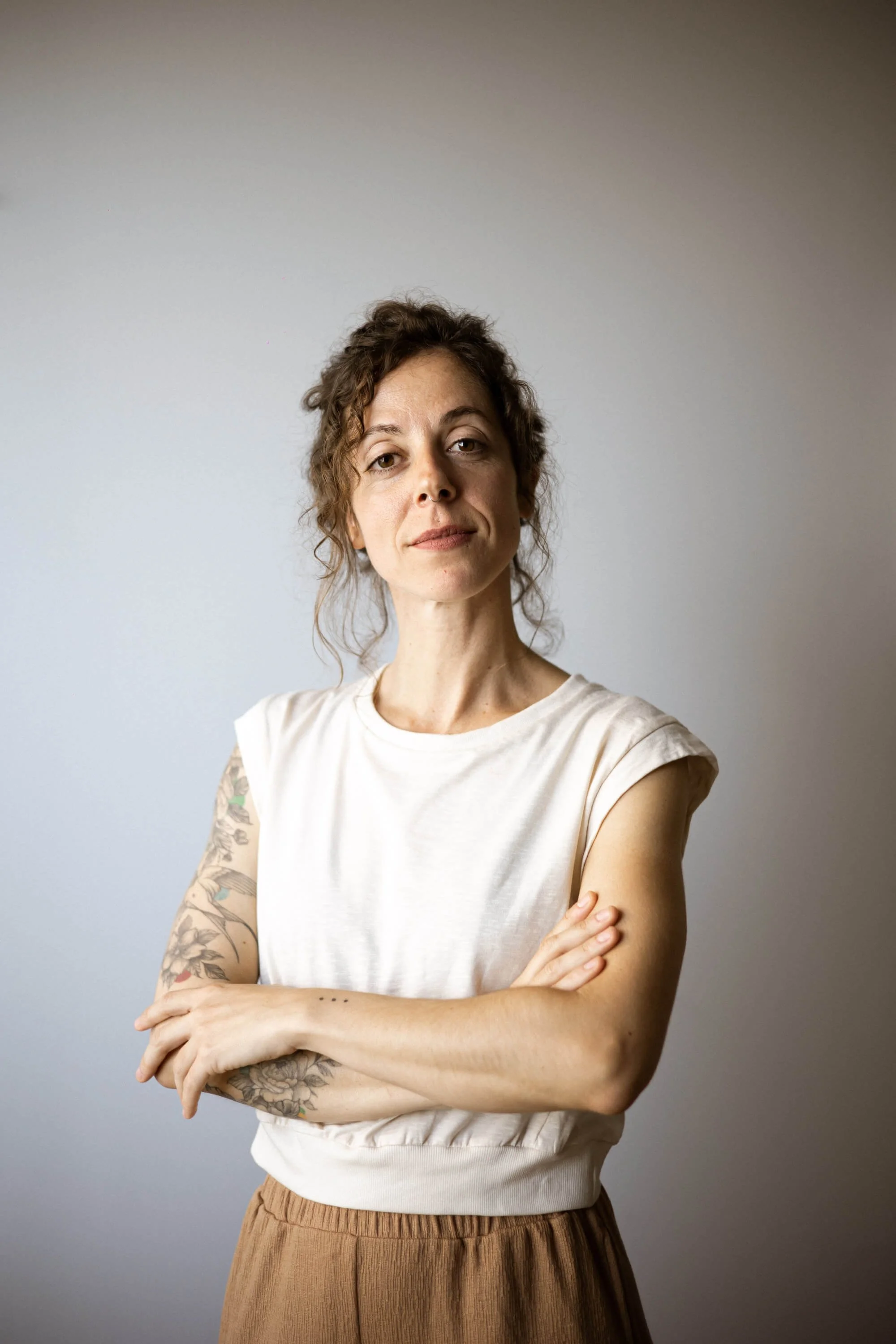 Alba de pie con brazos cruzados, en un fondo gris claro.