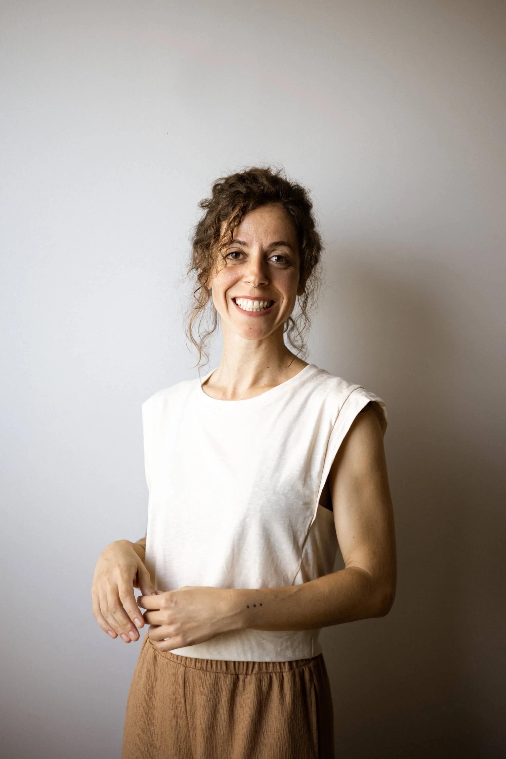 Alba sonriendo, con blusa blanca y pantalones beige, frente a fondo gris claro.