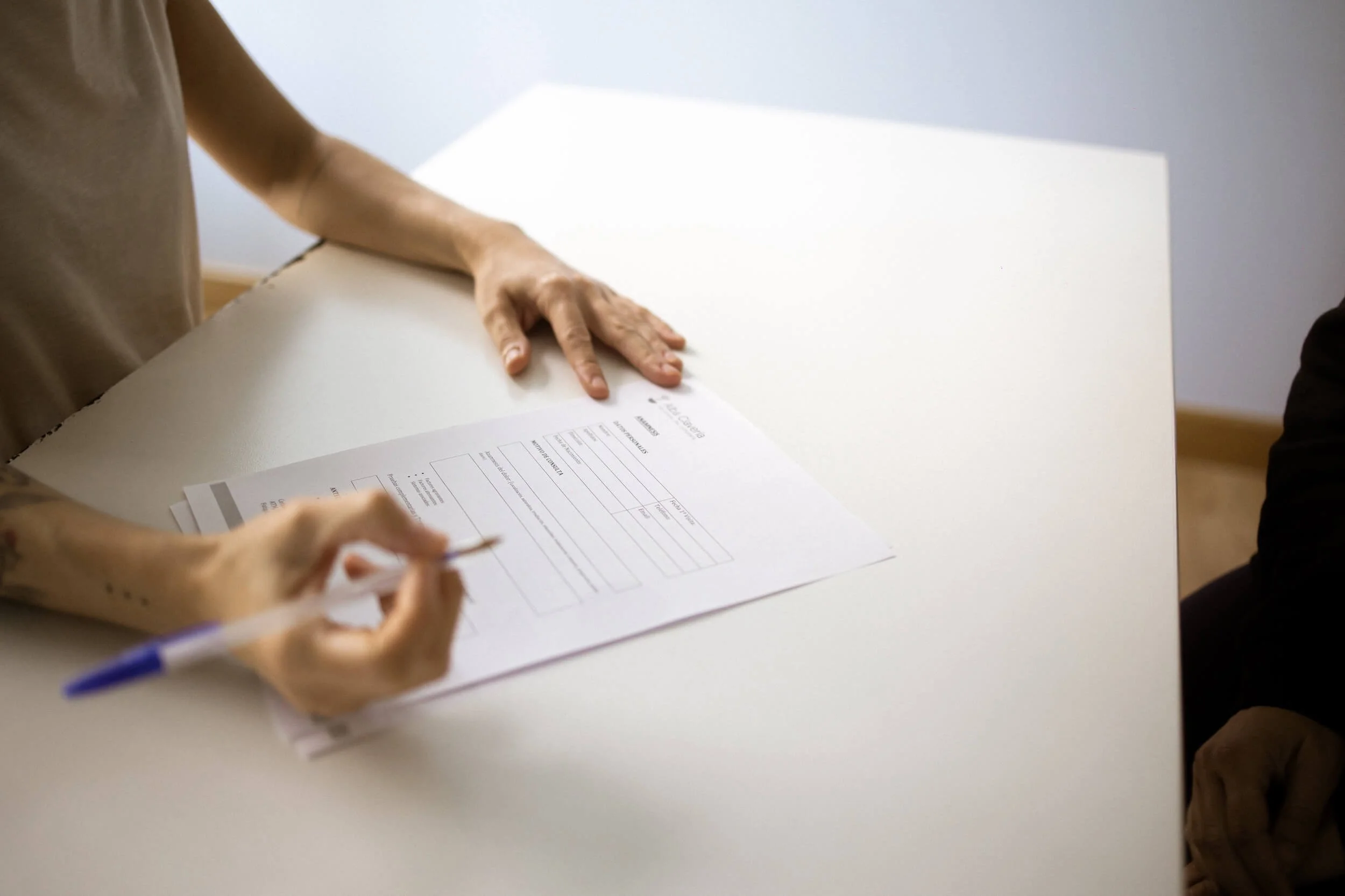 Persona llenando un formulario en una mesa blanca.