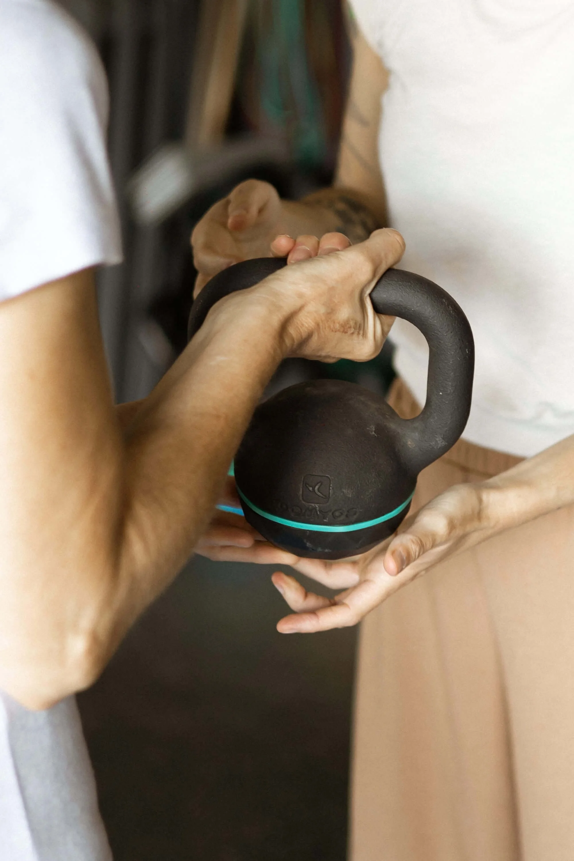Dos personas sosteniendo una pesa de kettlebell de color negro, una de ellas con una mano mayor y la otra con una mano más joven (de Alba).