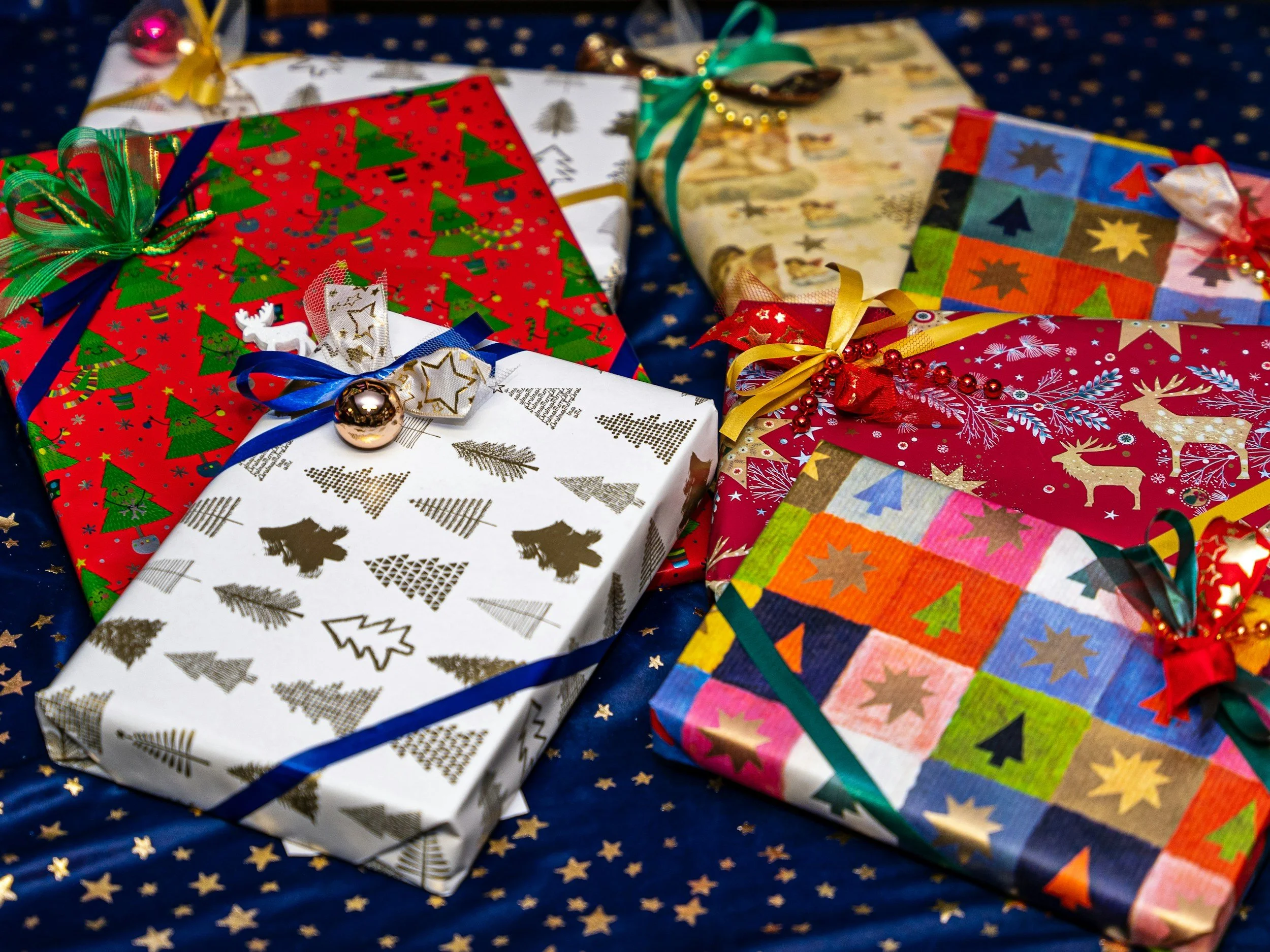 Multiple wrapped Christmas presents with festive wrapping paper and ribbons on a dark blue background with gold stars.
