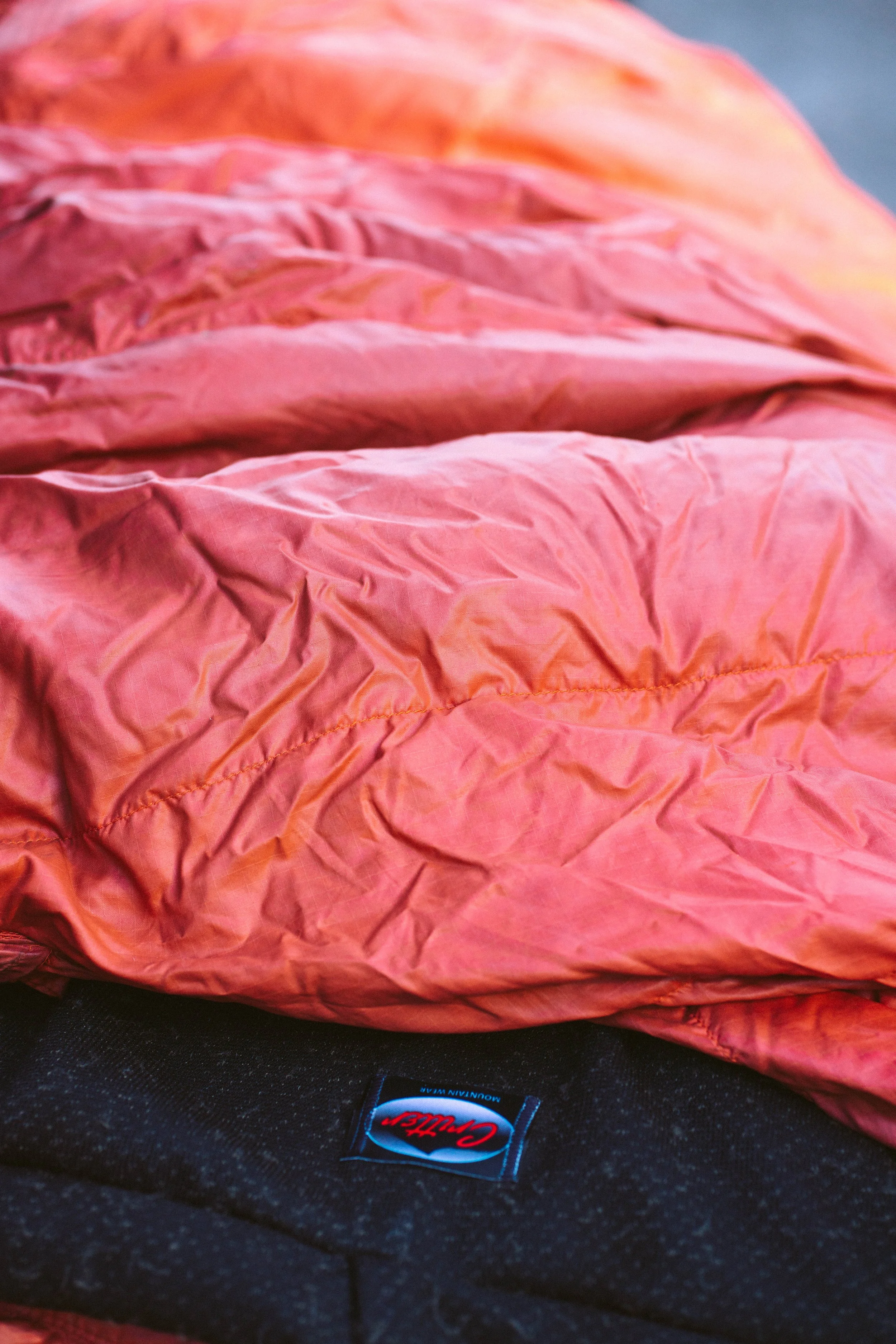 Close-up of a crumpled pink sleeping bag on a black surface with a small logo that reads 'CRITTER MOUNTAIN WEAR'.