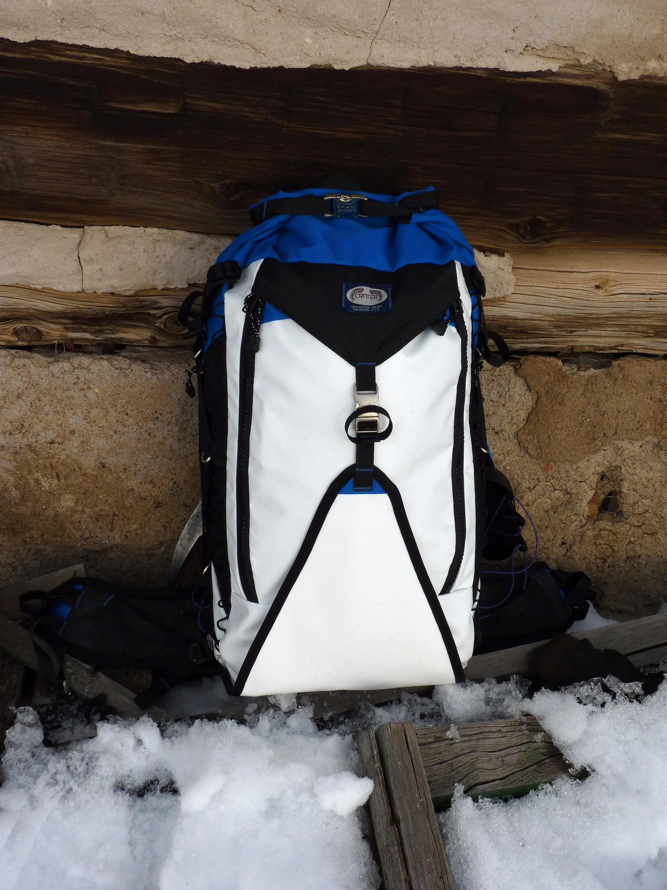 A white, blue, and black backpack with a black zipper and a black buckle. The backpack has a white front panel with a black trim and a blue strap.