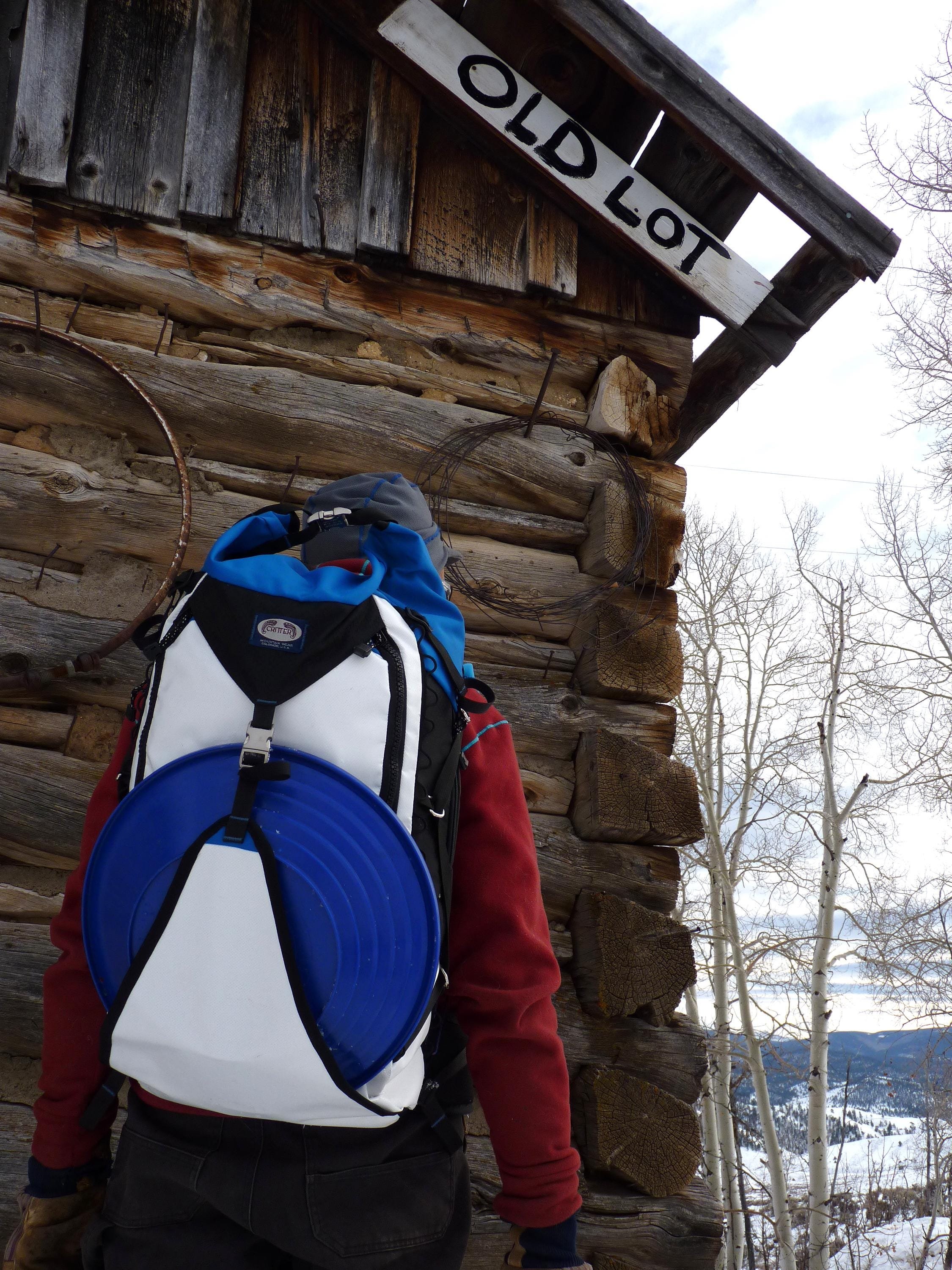 A white and blue backpack with a large, round, blue gold pan attached to the front.
