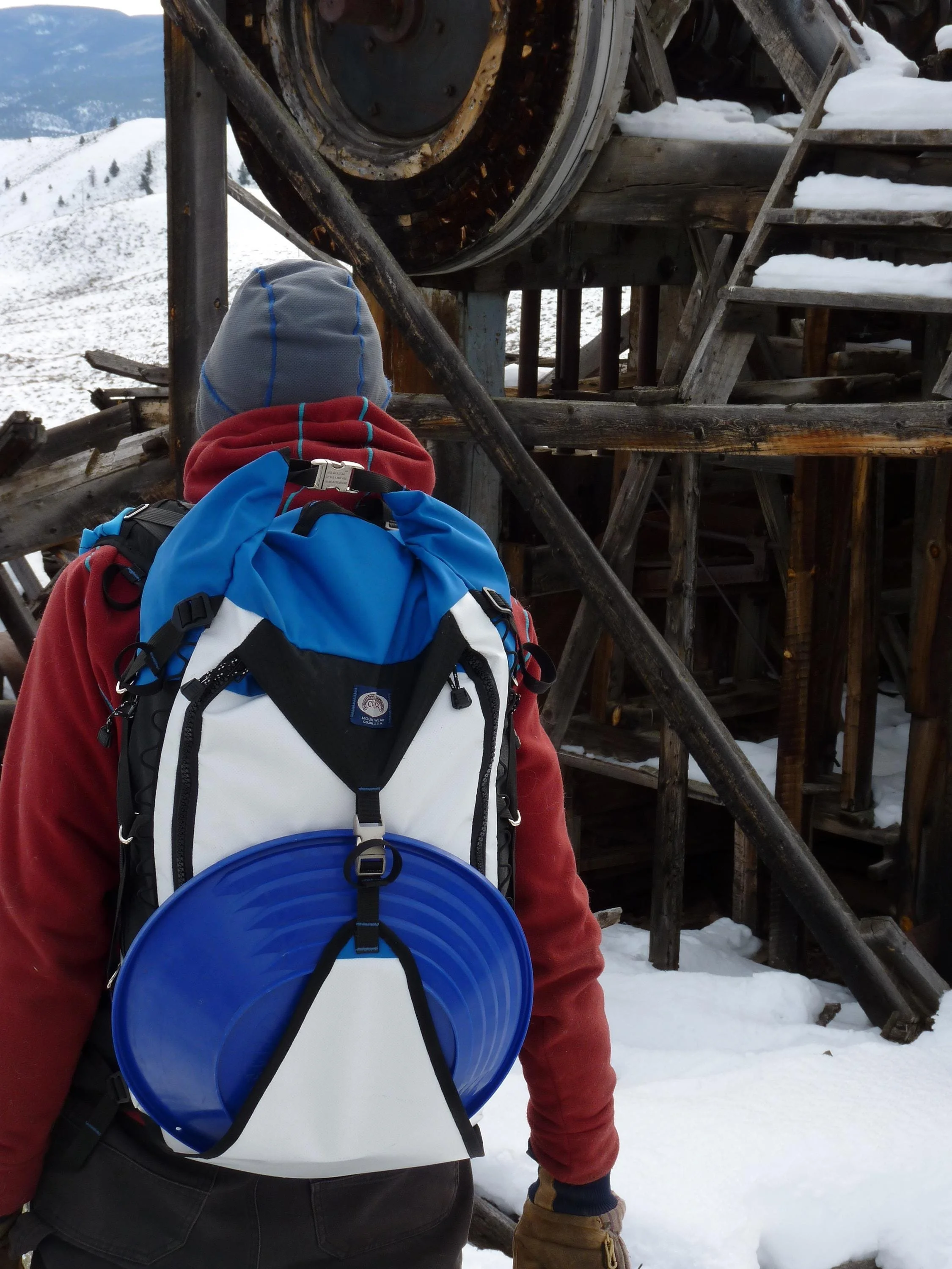 A white and blue backpack with a blue gold pan attached to the front. The backpack has black straps and a black zipper.