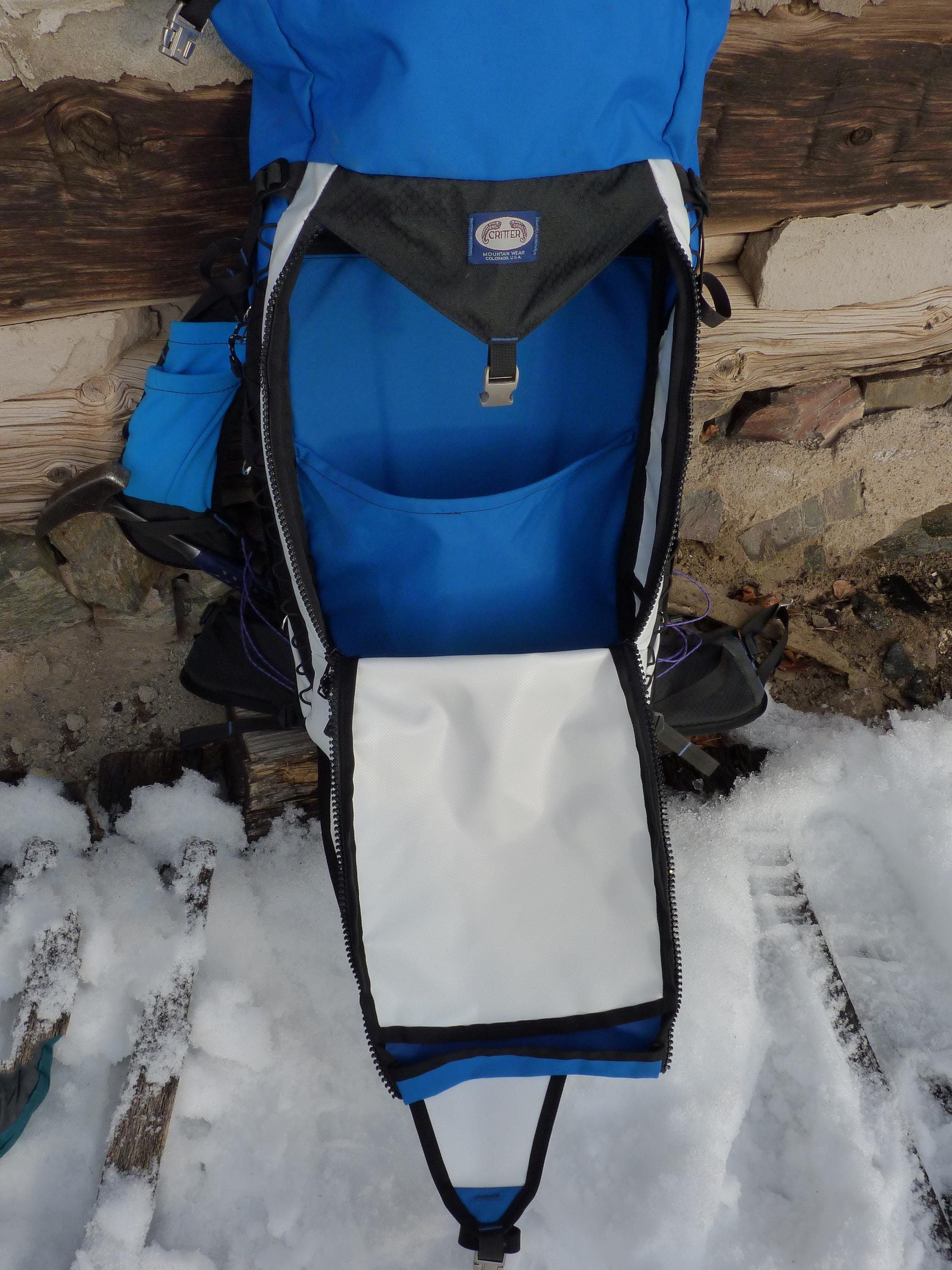 A blue and white backpack with a white zippered pocket on the front. The backpack is open and the inside is white.