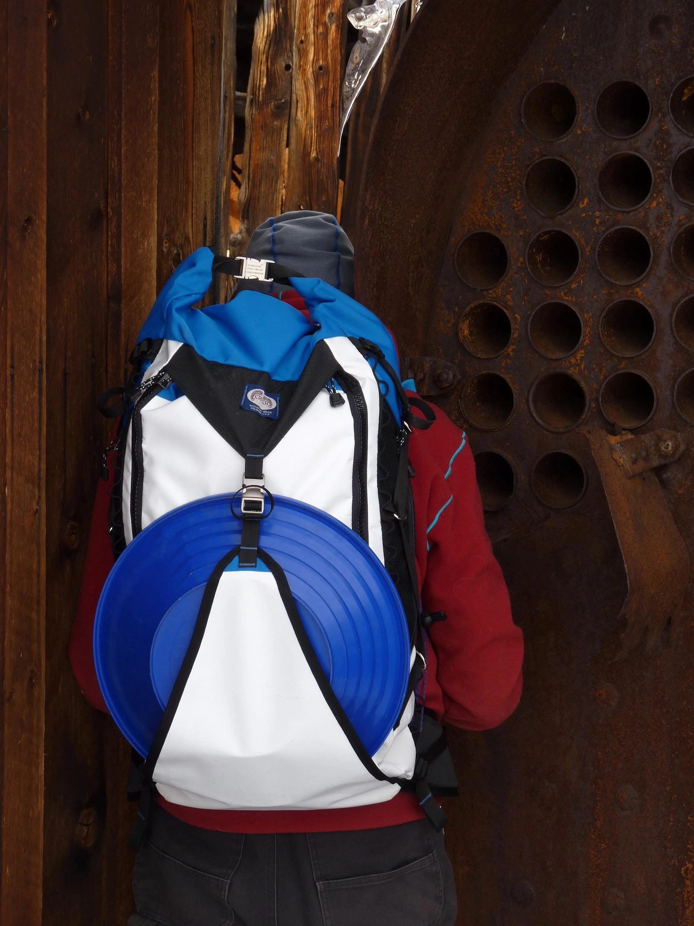 A blue and white backpack with a blue disc attached to the back. The backpack has a black zipper and black straps.