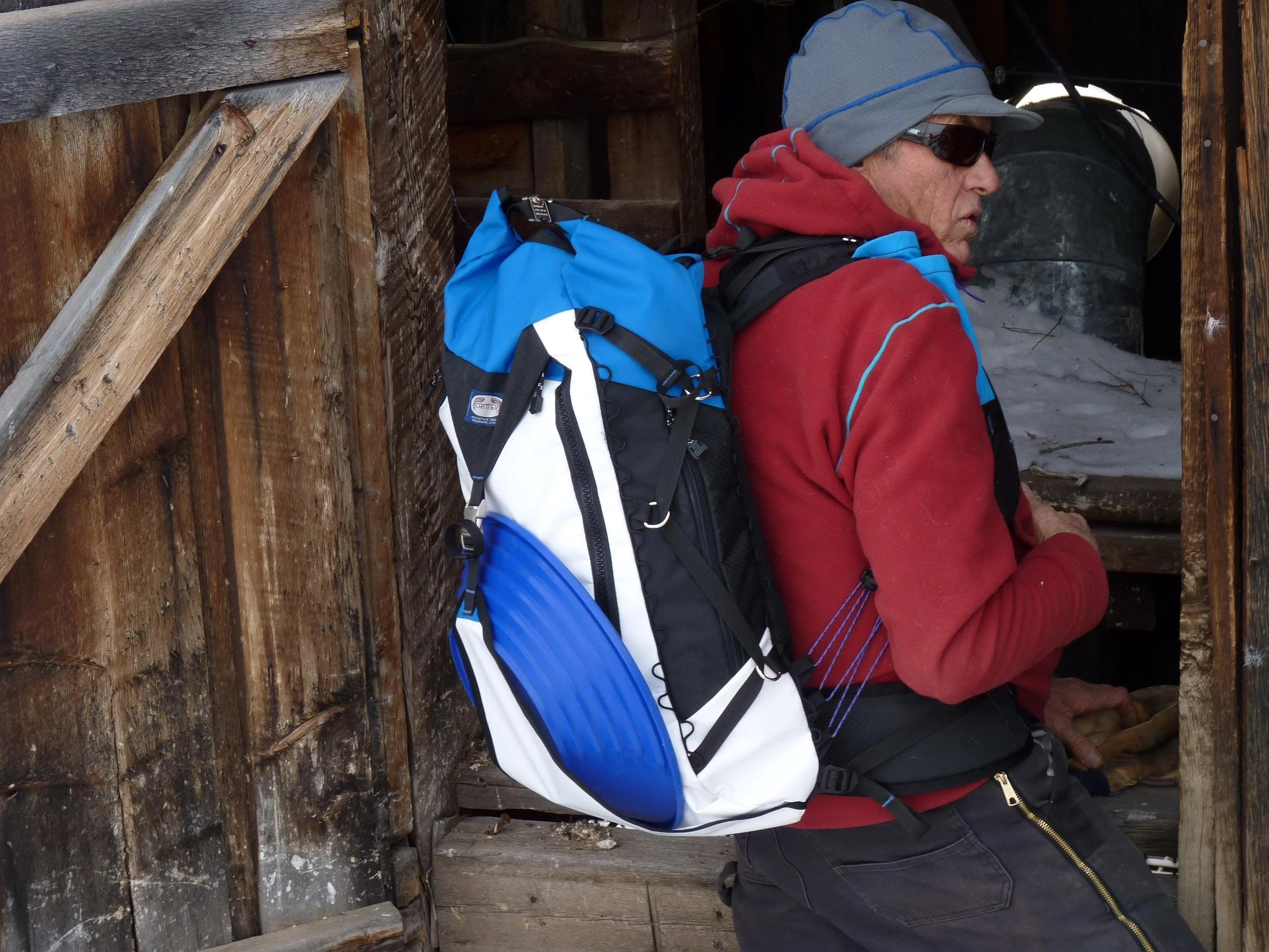 A blue, white, and black backpack with a blue and white front panel. The backpack has a large main compartment and a smaller front pocket.