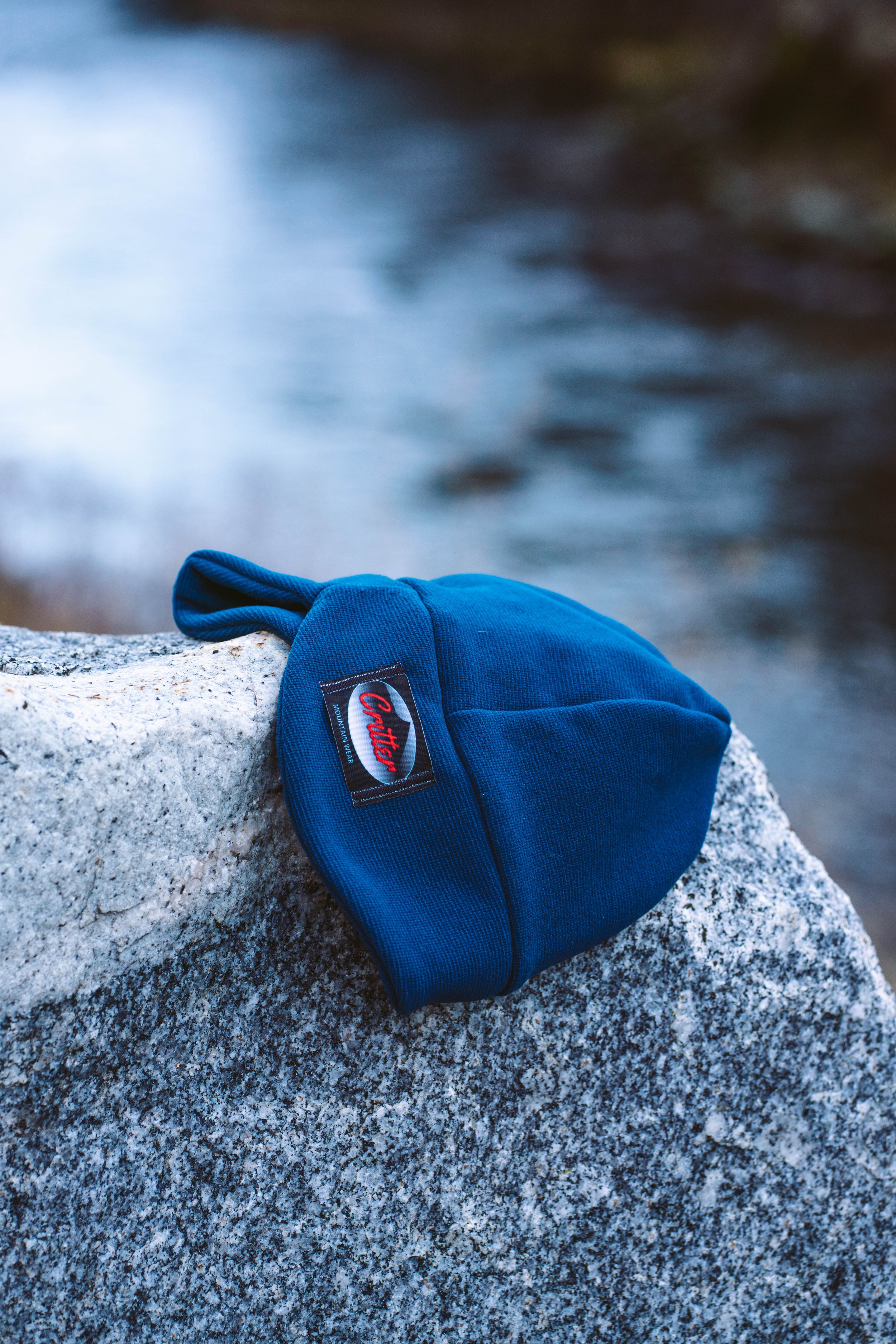 A blue mountain biking cap resting on a gray rock near a body of water.