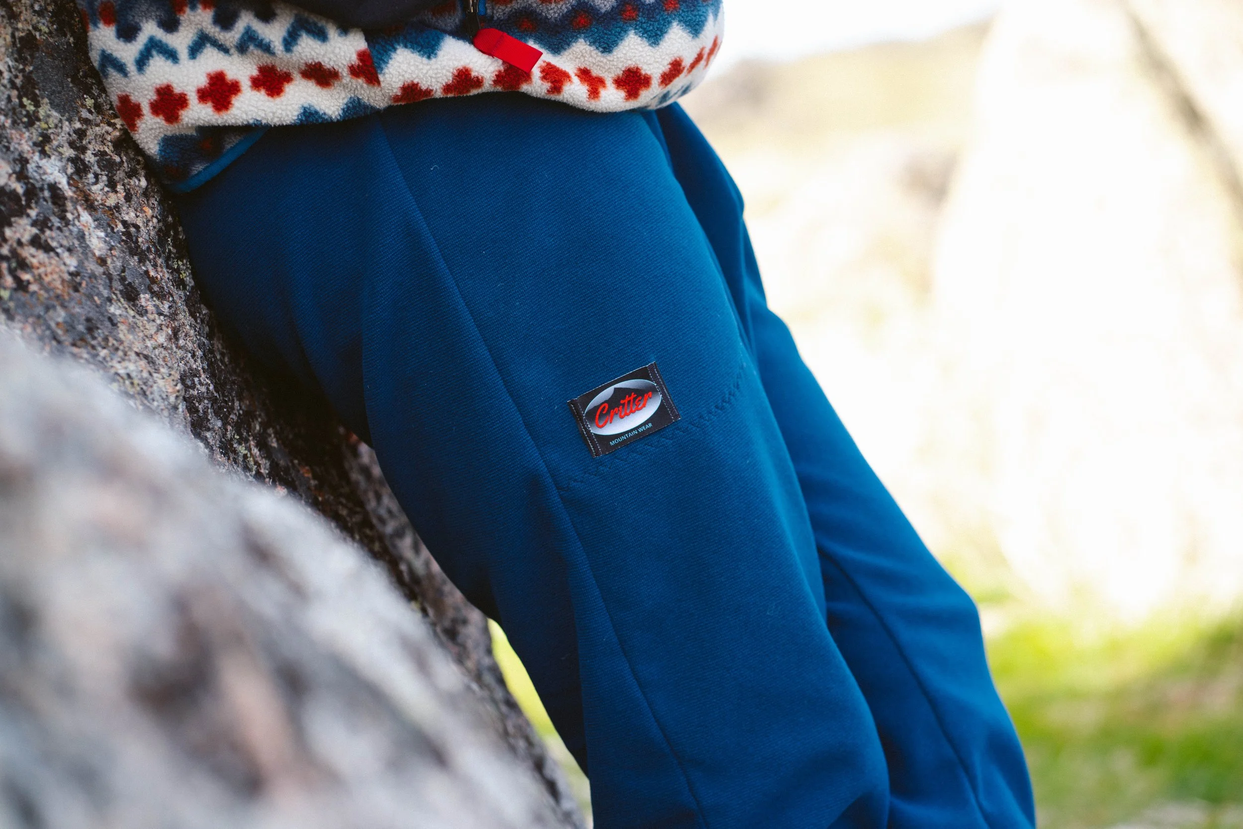 A person wearing a pair of Critter pants with their hands in the pockets while leaning against a rock.