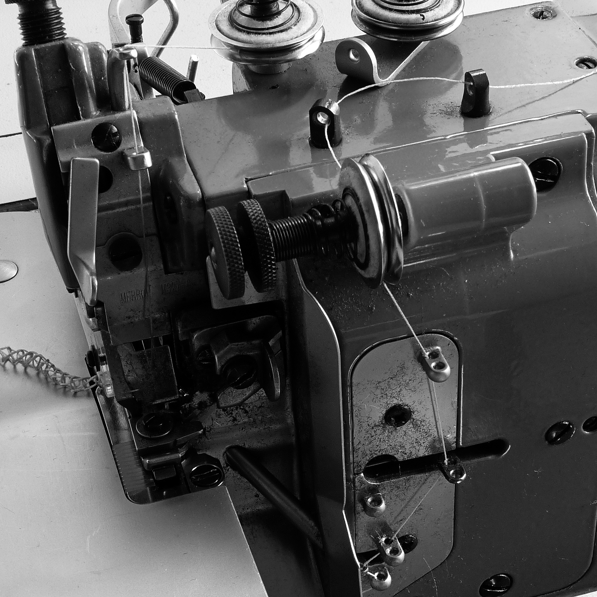 Close-up of a vintage sewing machine showing metal parts, tension mechanisms, and thread spools in black and white.