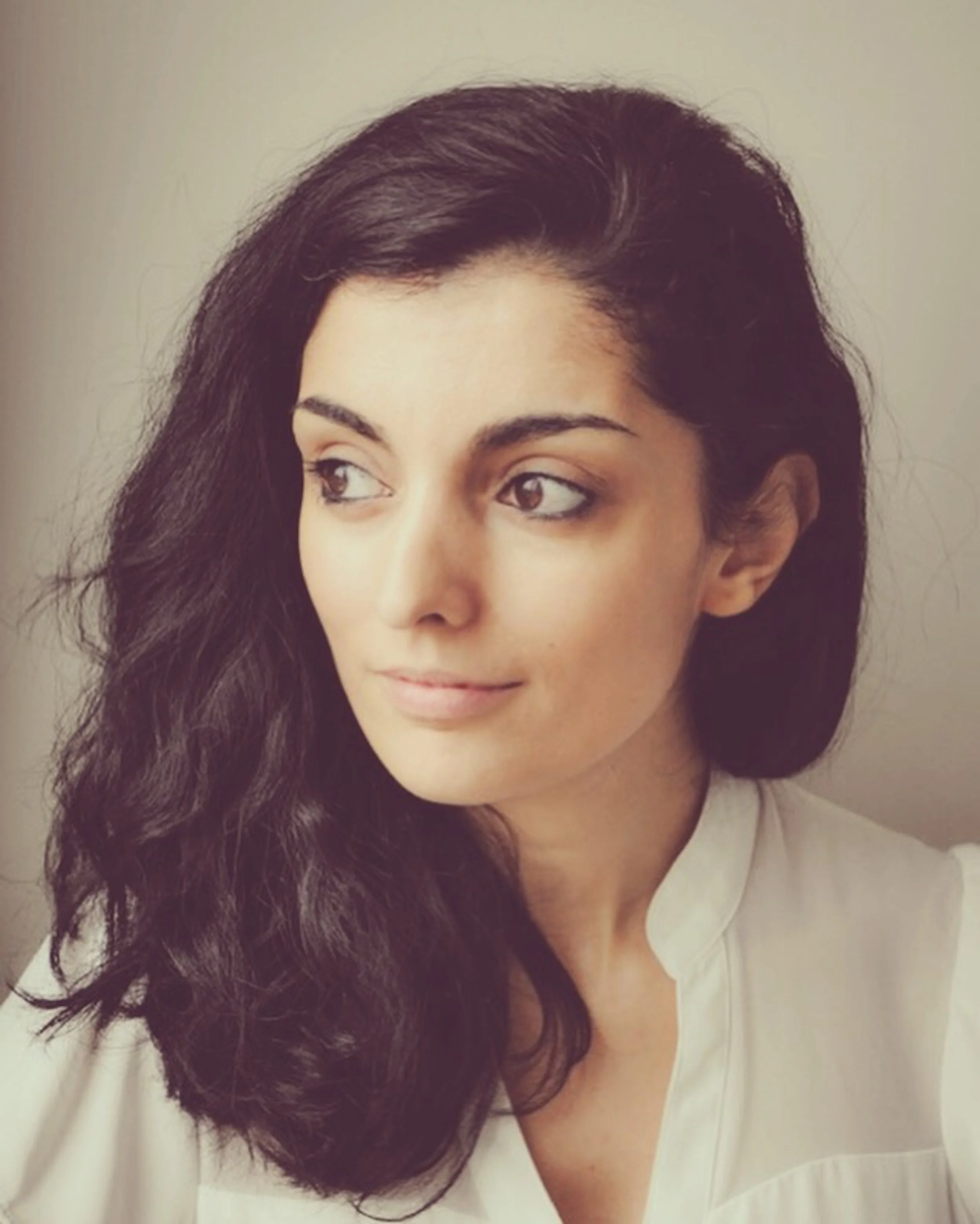 A woman with long, dark, wavy hair looking to the side in a neutral expression.