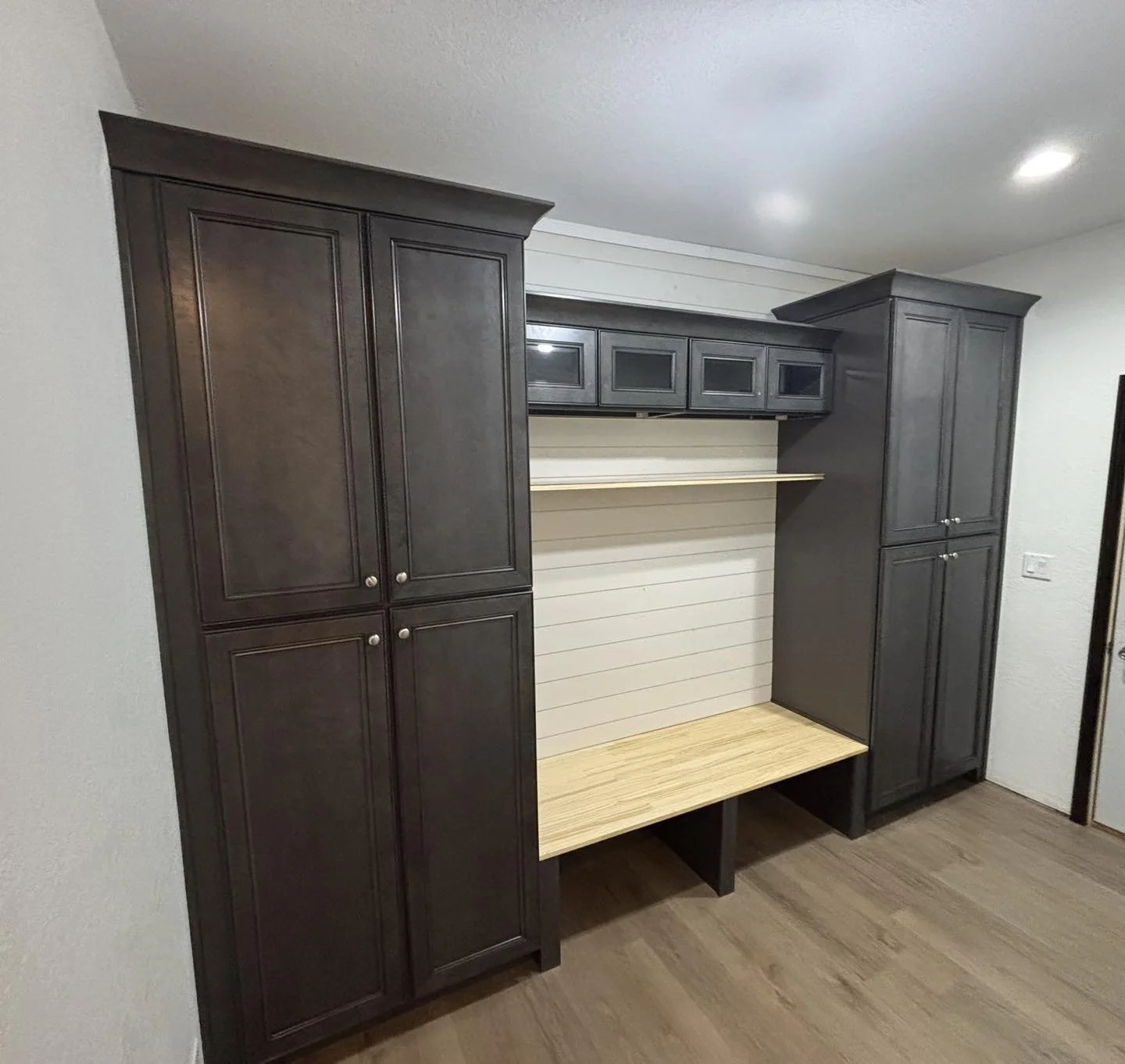 A built-in dark gray cabinet with storage, open shelves, and a wooden bench in front, against a white wall with horizontal paneling.