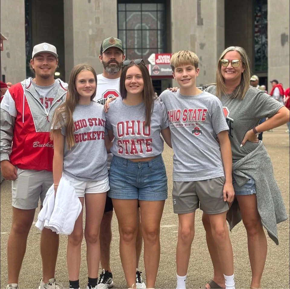 Group of six people, wearing Ohio State Buckeyes apparel, standing together outside a stadium.