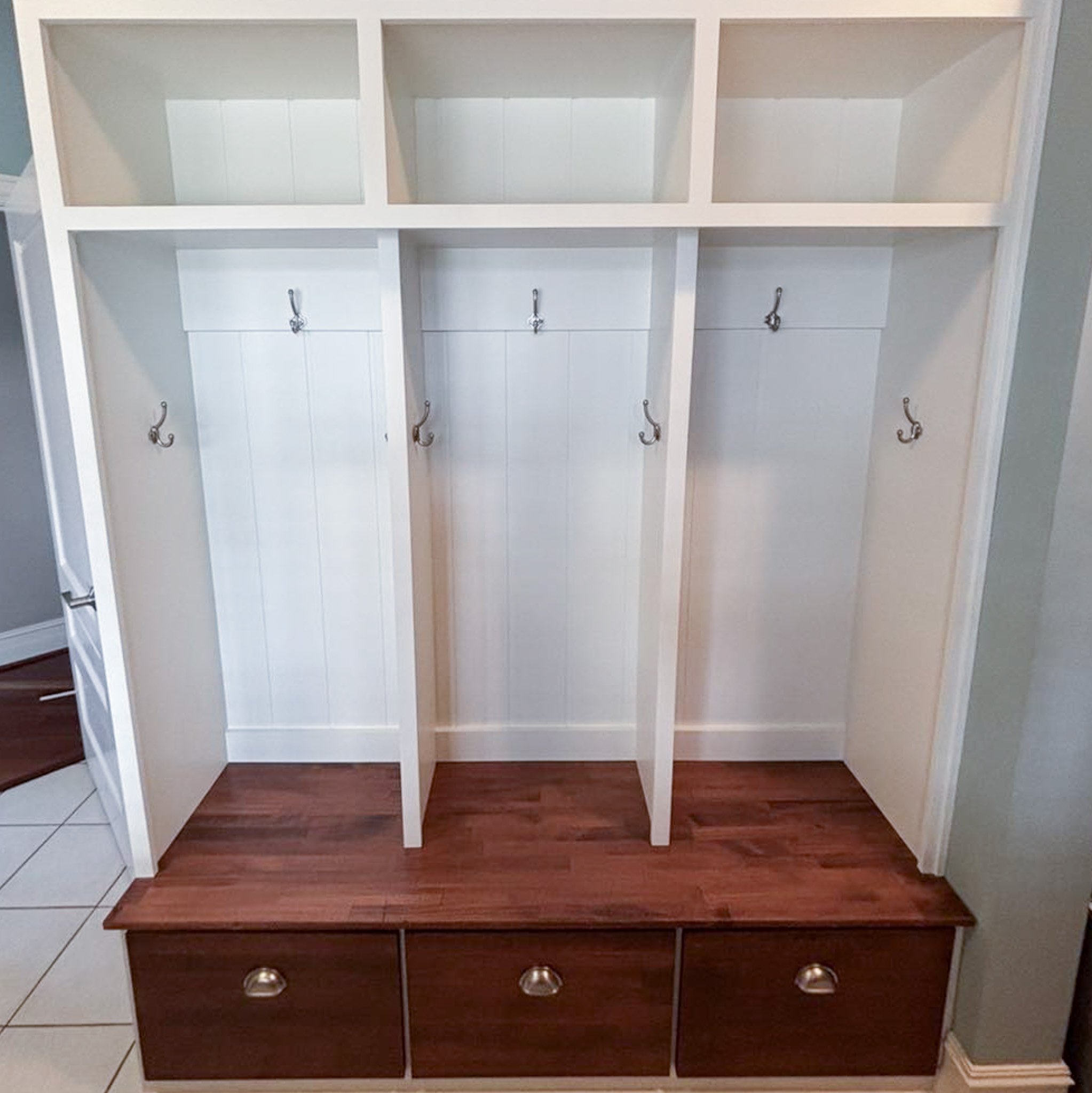 A white hall tree with hooks for coats and a wooden bench with drawers at the bottom.
