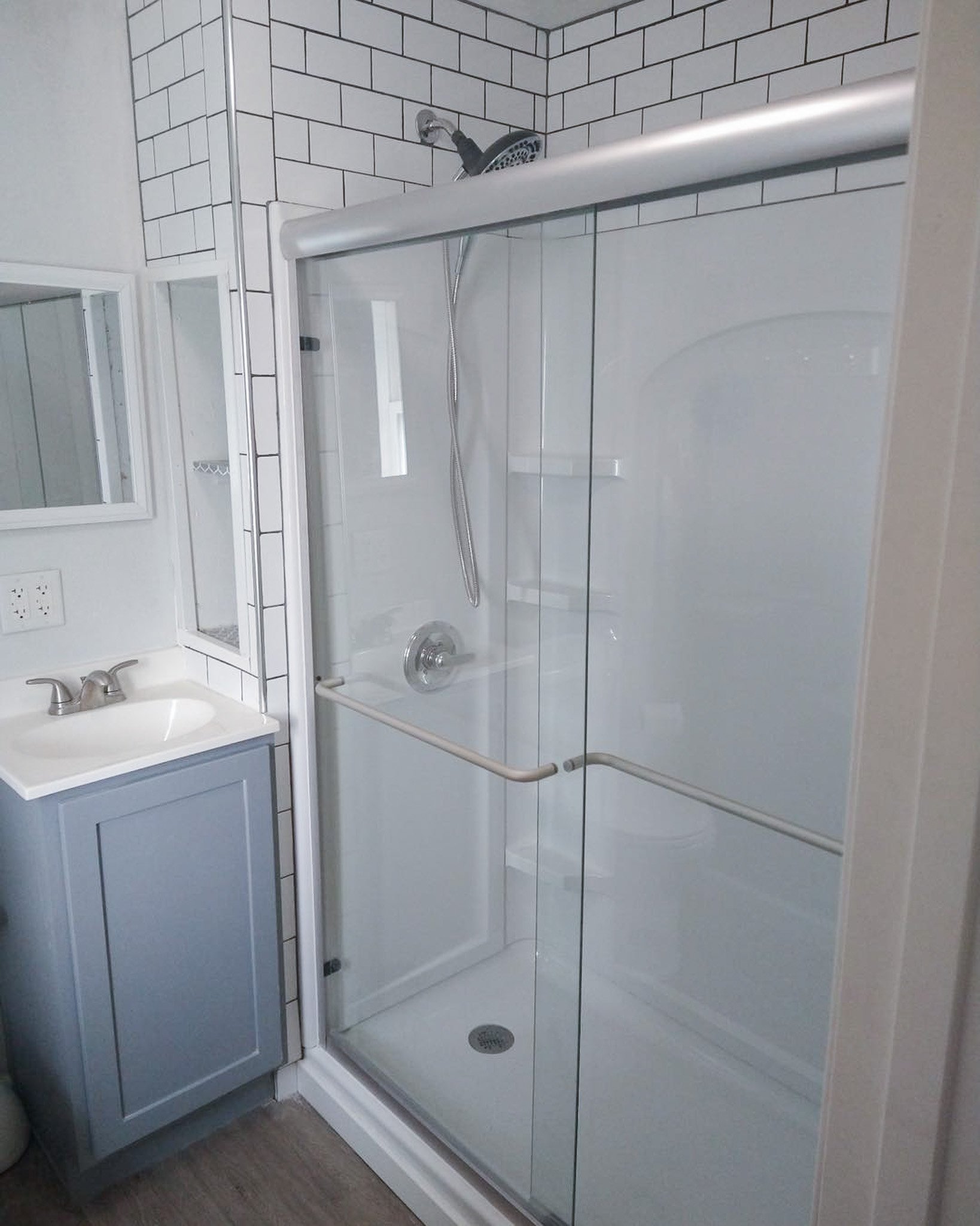 Bathroom with walk-in shower, glass door, white tile walls, small vanity with sink, mirror, and a window.