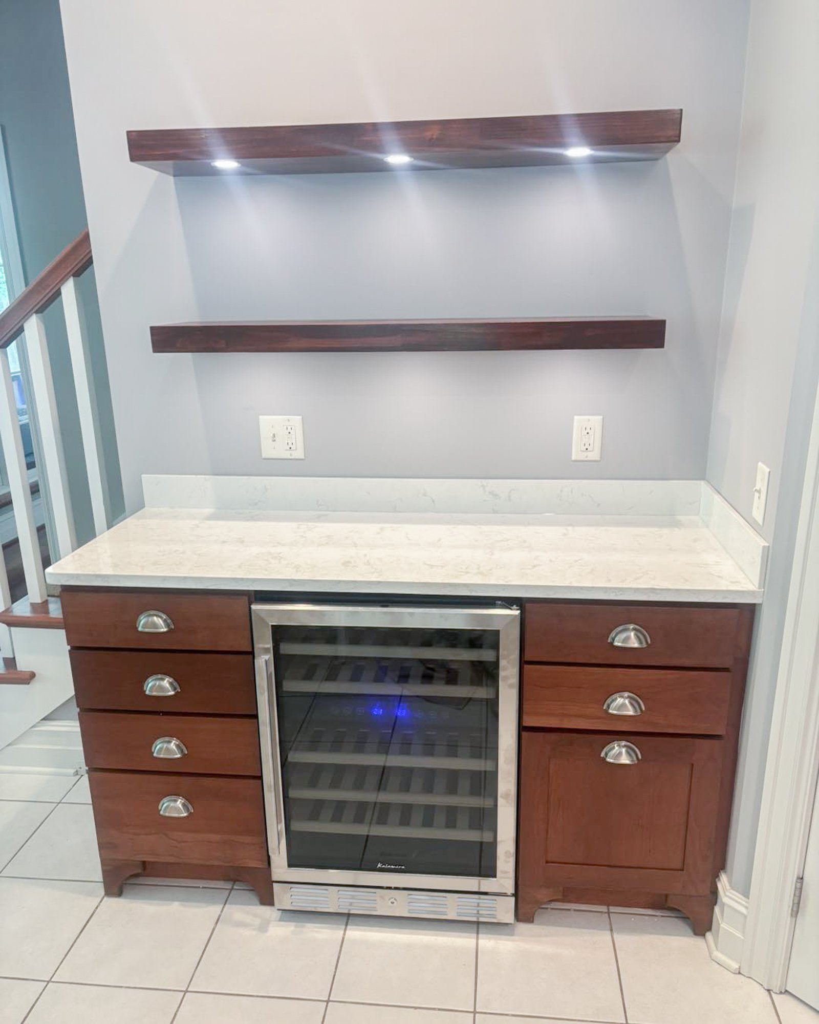 Kitchen cabinet with marble countertop, wine cooler, and two wooden shelves mounted on a gray wall.