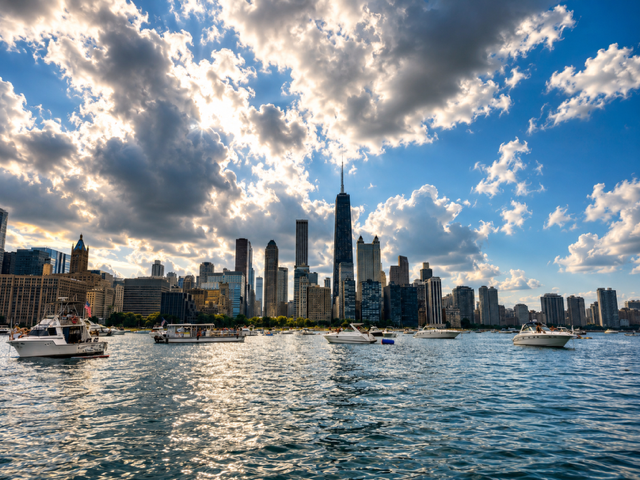 View of the New York City skyline from the water with boats in the foreground and partly cloudy sky.