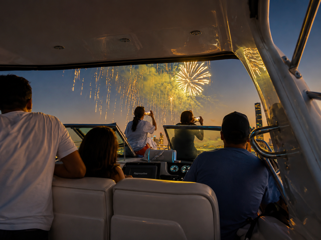 People on a boat watching fireworks display at night.