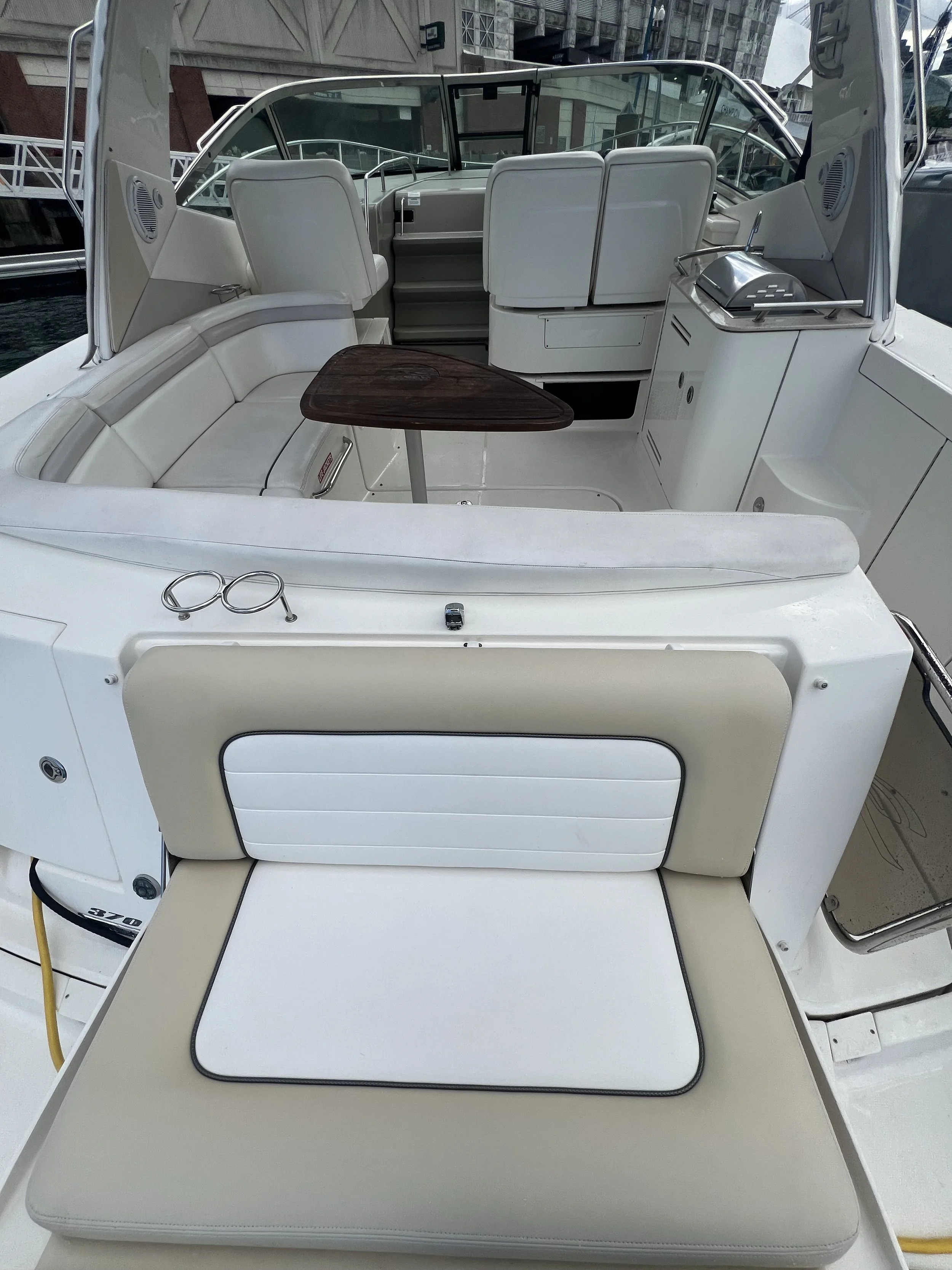 The image shows the interior of a boat, including white cushioned seats, a small wooden table, a built-in grill, and various equipment and storage compartments.