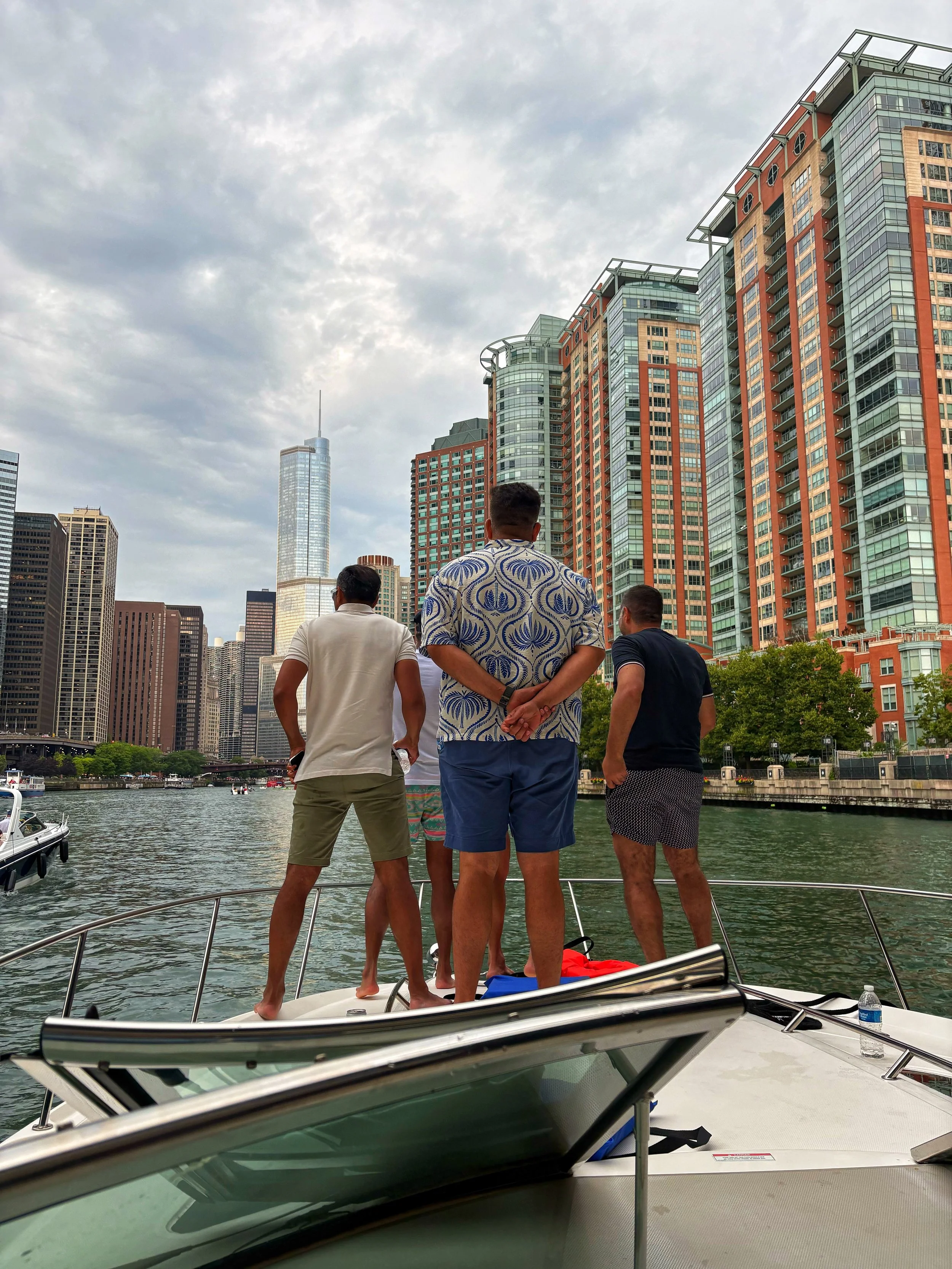 People standing on a boat in a city with tall buildings and skyscrapers along the water, with some boats visible in the water.