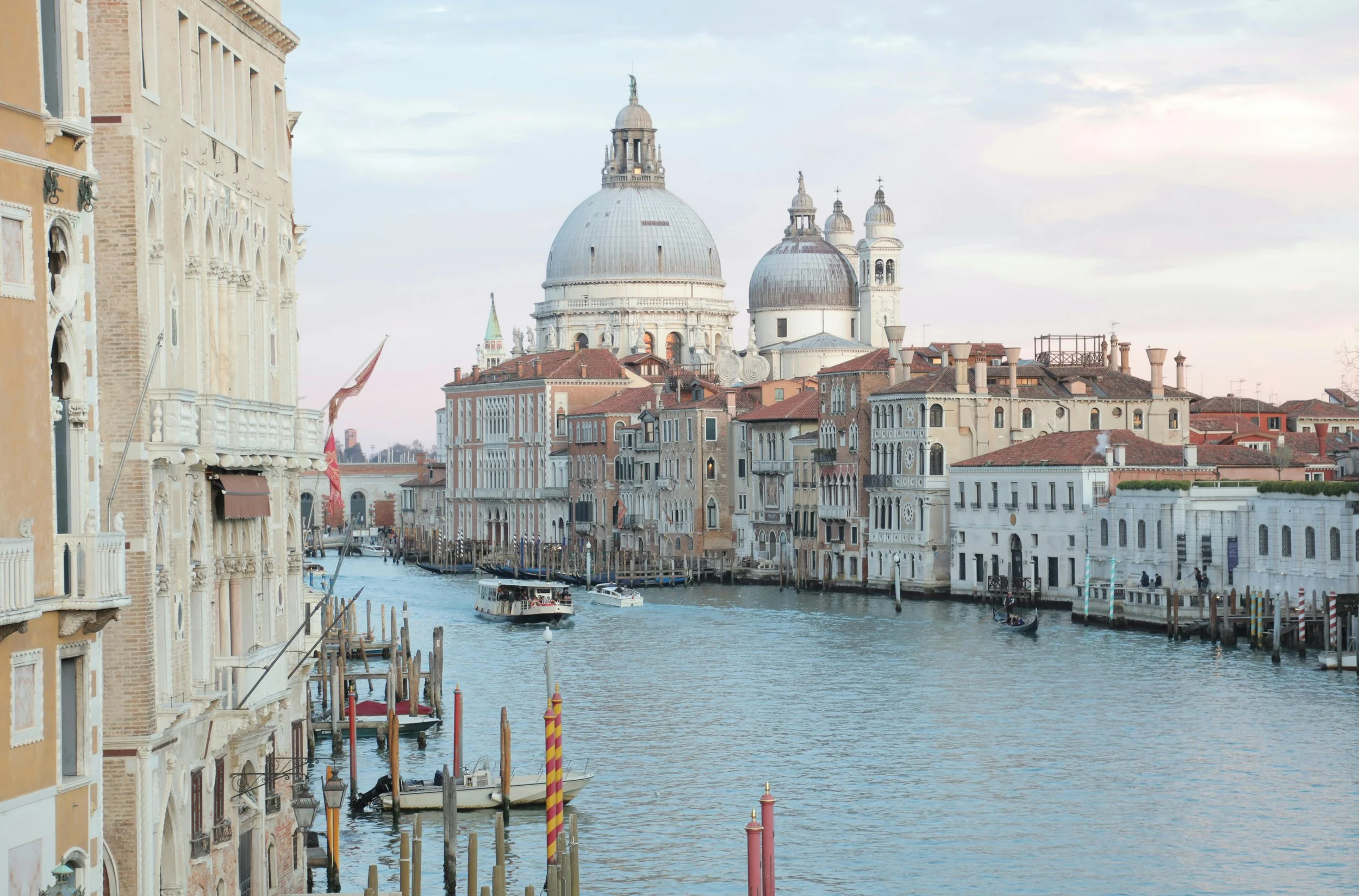 View of the Grand Canal in Venice, Italy, with historic buildings and domes in the background, boats on the water, and pastel-colored facades along the canal.