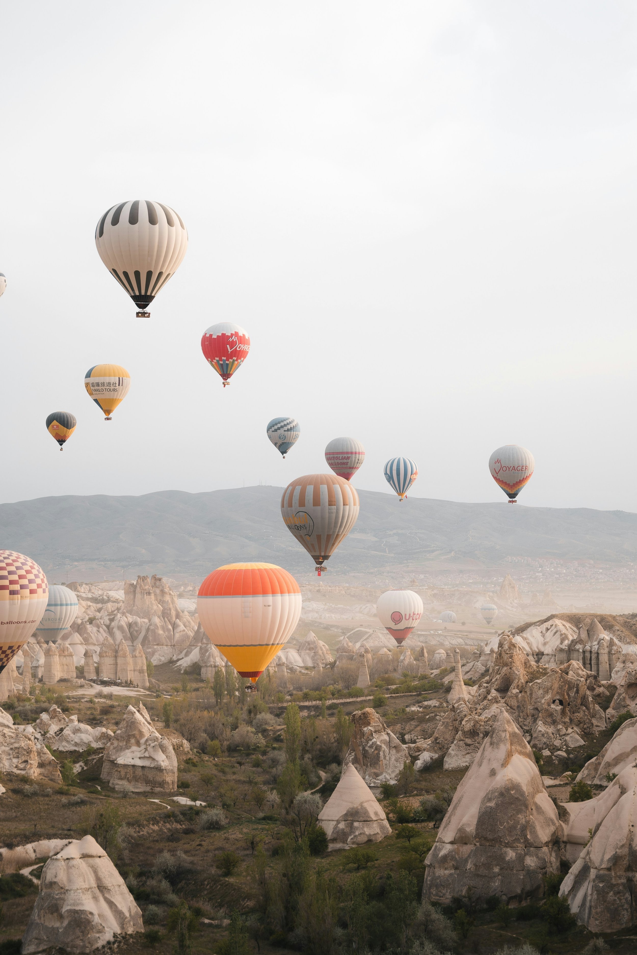 Multiple hot air balloons floating over a rocky landscape with unique rock formations, under a cloudy sky.