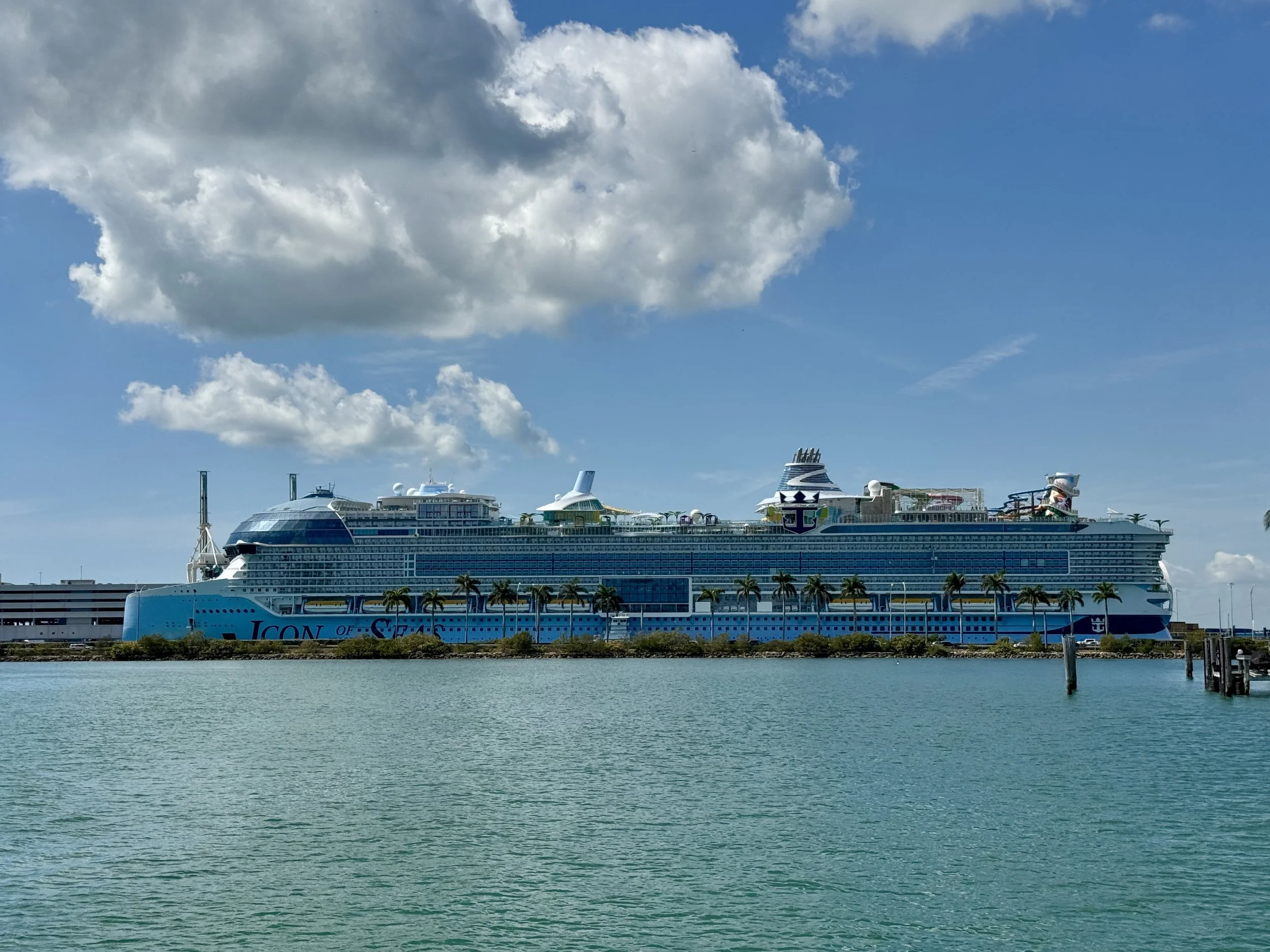 Large cruise ship named ICON of the Seas docked at a port with calm water and a partly cloudy sky.