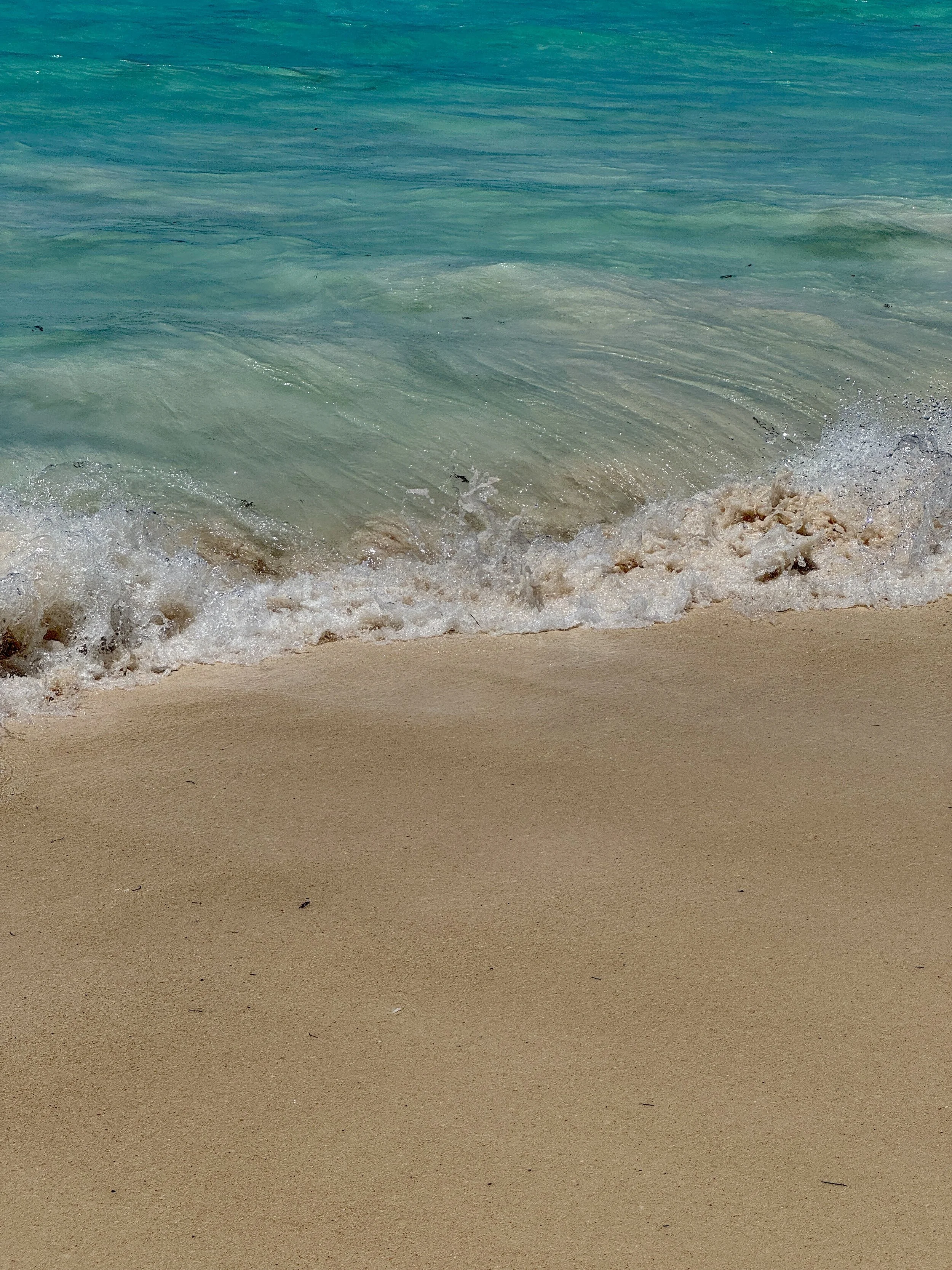 Close-up of ocean waves gently hitting a sandy beach with aqua-colored water.