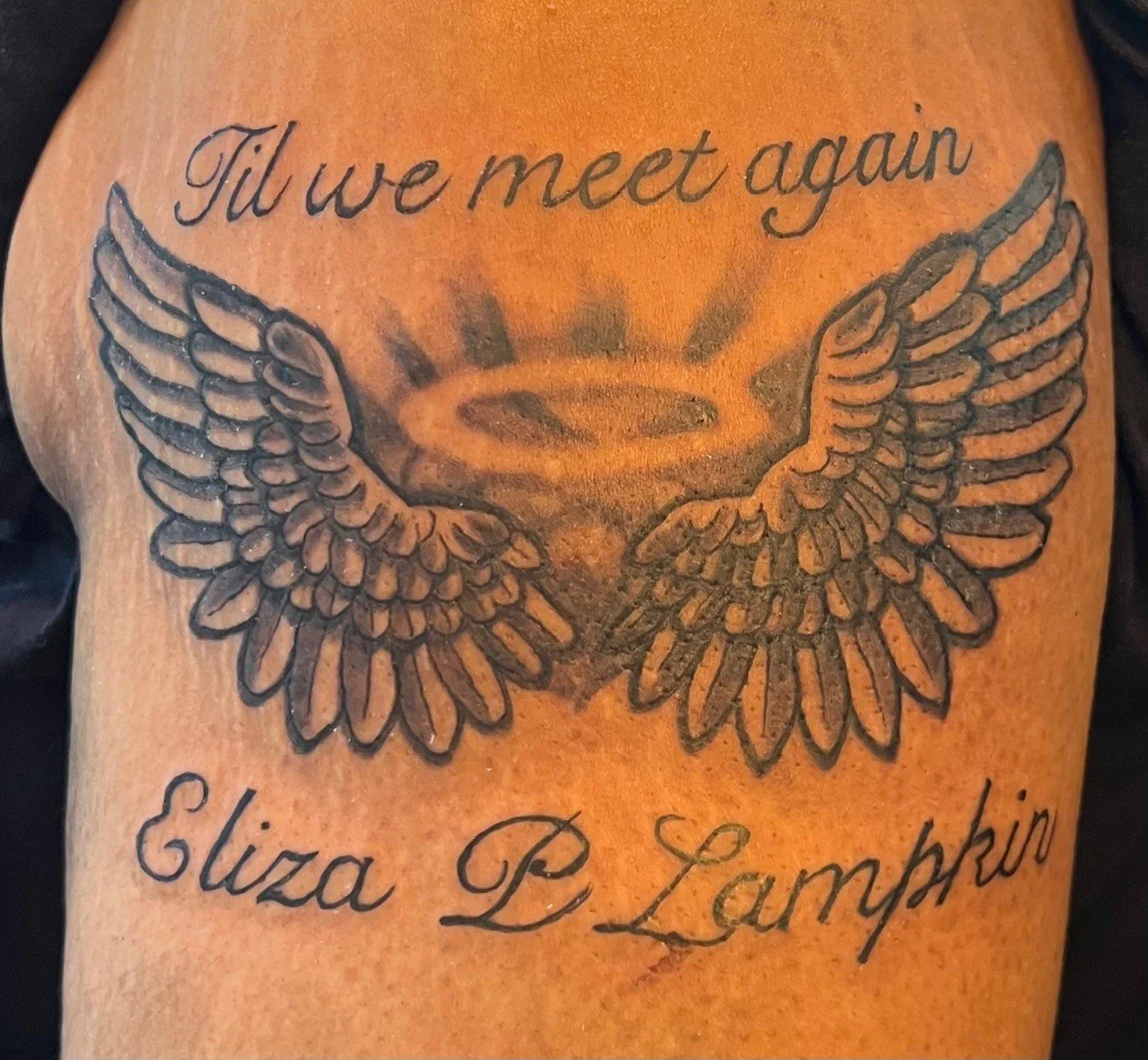 Tattoo of angel wings surrounding a halo with the text 'Til we meet again' and 'Eliza P. Lamkin' written above and below.