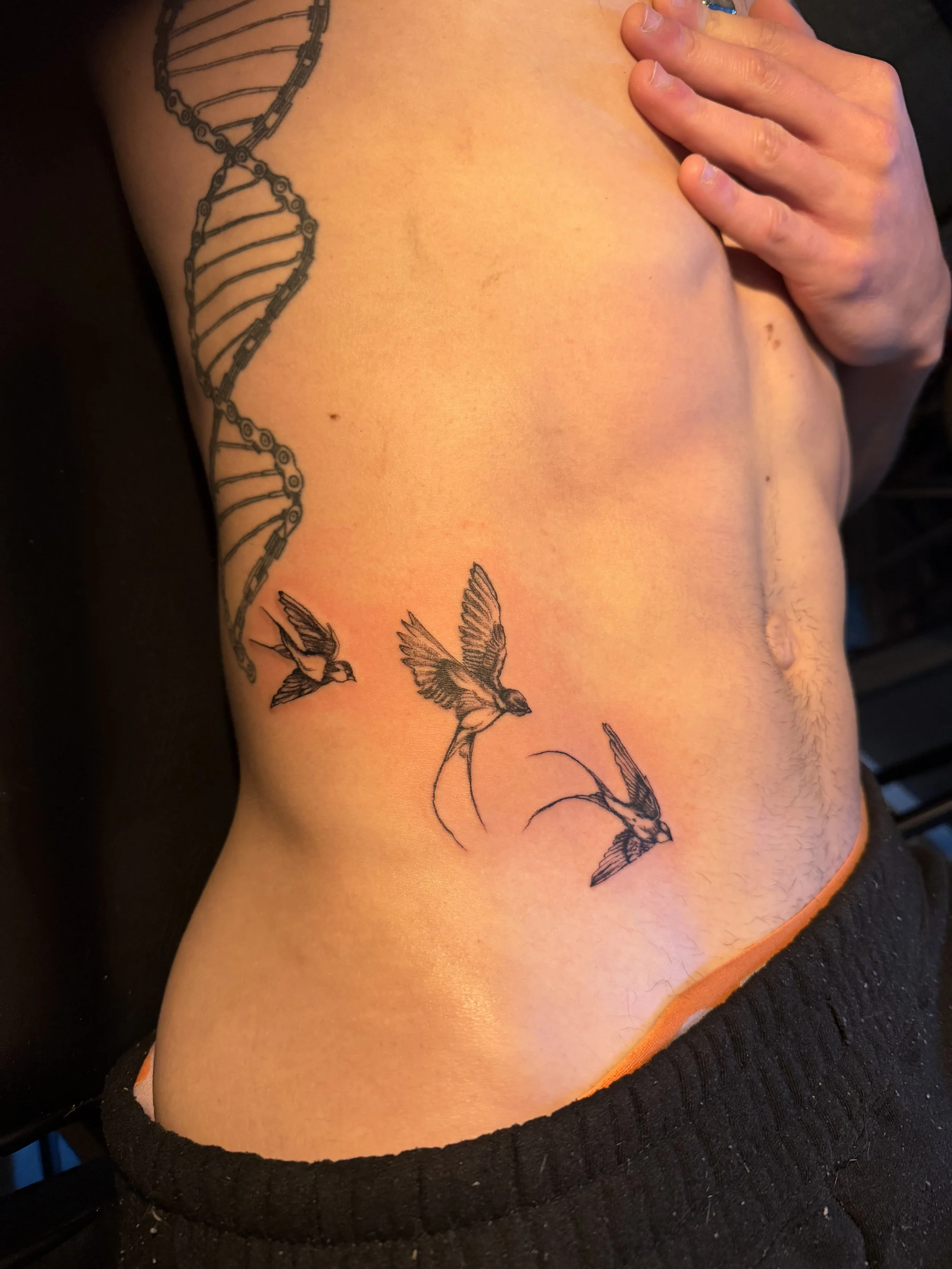 A person's back shows a large tattoo of a DNA double helix with birds flying near the bottom.