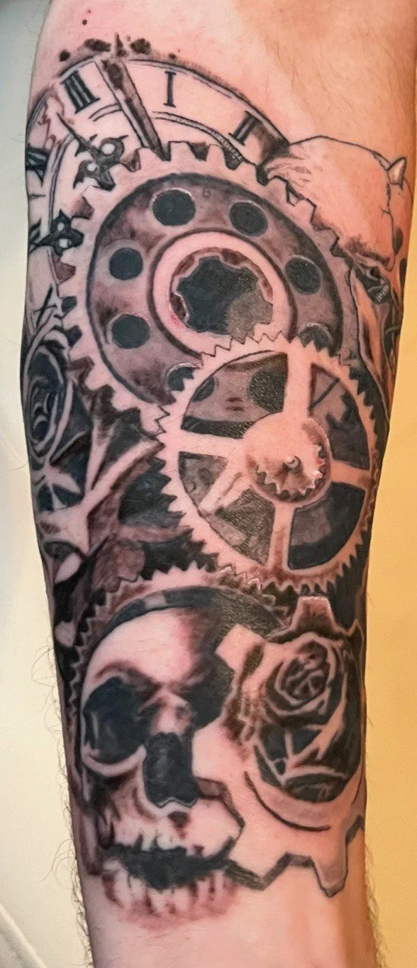 Tattoo featuring clock gears, a human skull, and a rose on a person's arm.