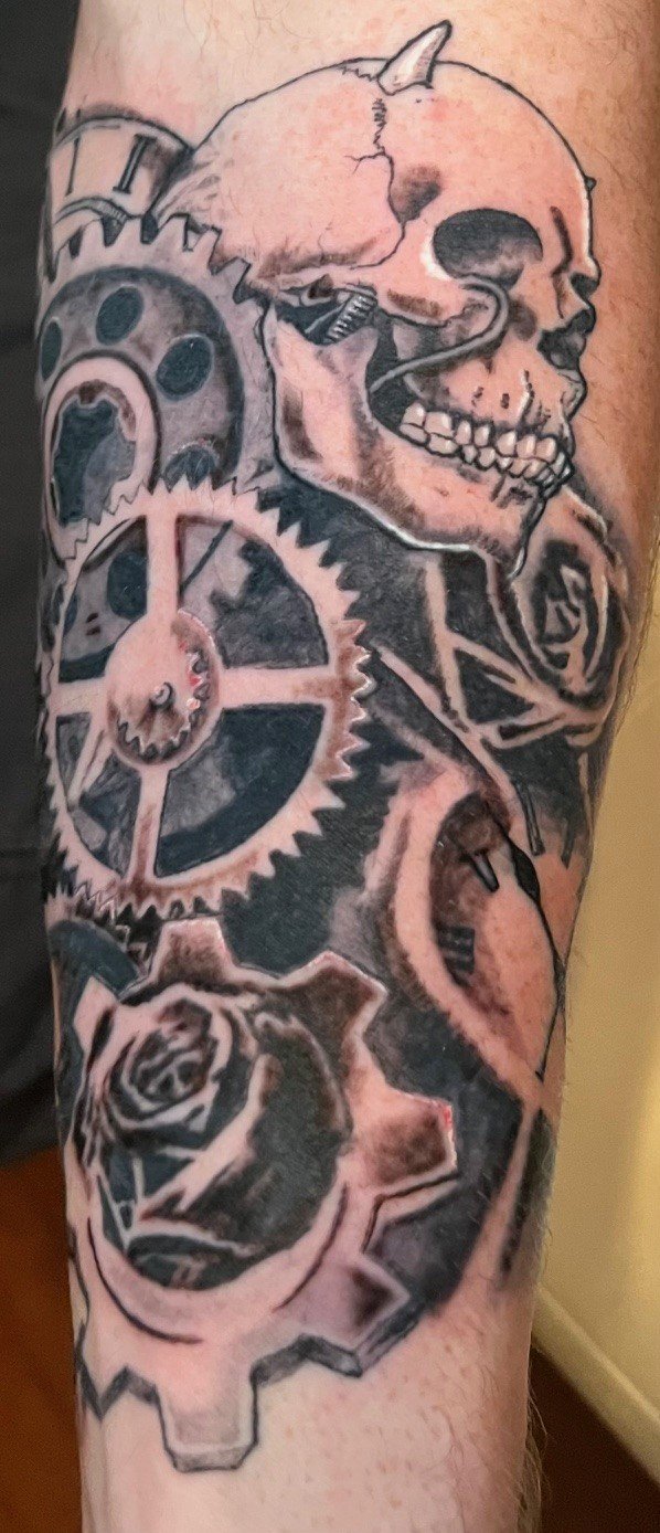 Tattoo of a human skull, gears, a clock, and a rose.