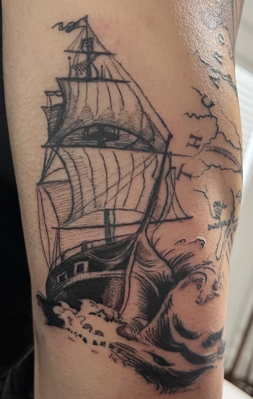 A black ink tattoo of a sailing ship with detailed sails set against a map background on skin.