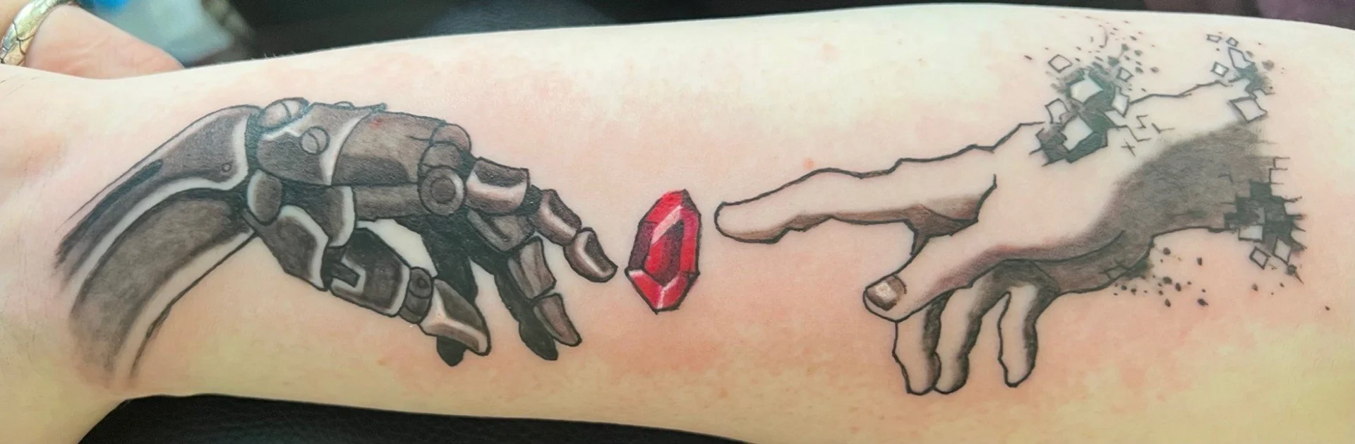 Tattoo of two hands reaching towards each other, reminiscent of Michelangelo's Sistine Chapel ceiling, with one hand depicted as robotic and the other as a realistic human hand, with a red gemstone floating between them.