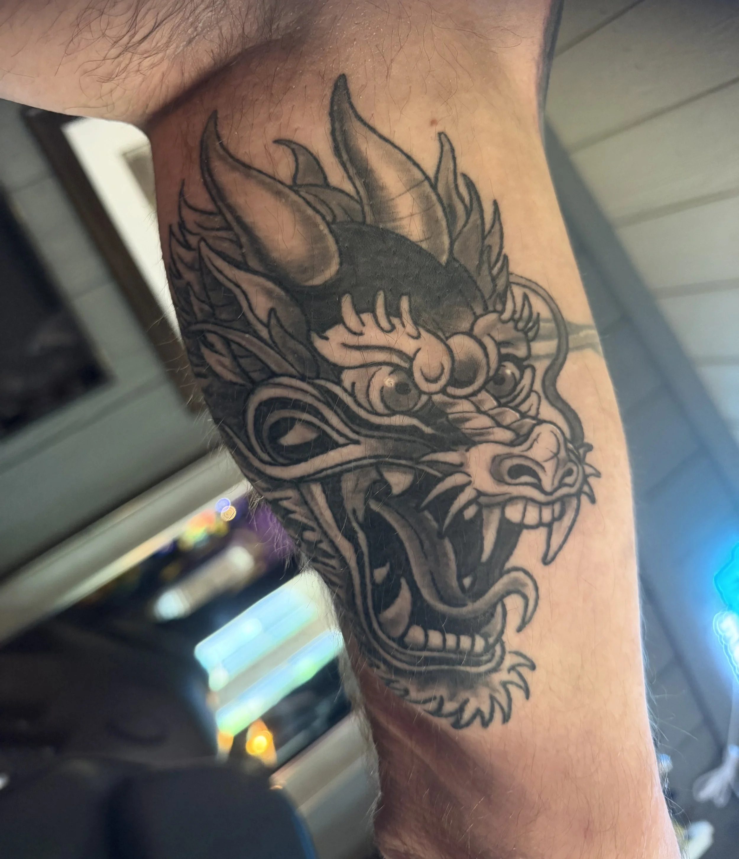 Close-up of a person's leg with a detailed tattoo of a dragon, showing scales and flames, with a colorful object in the foreground.