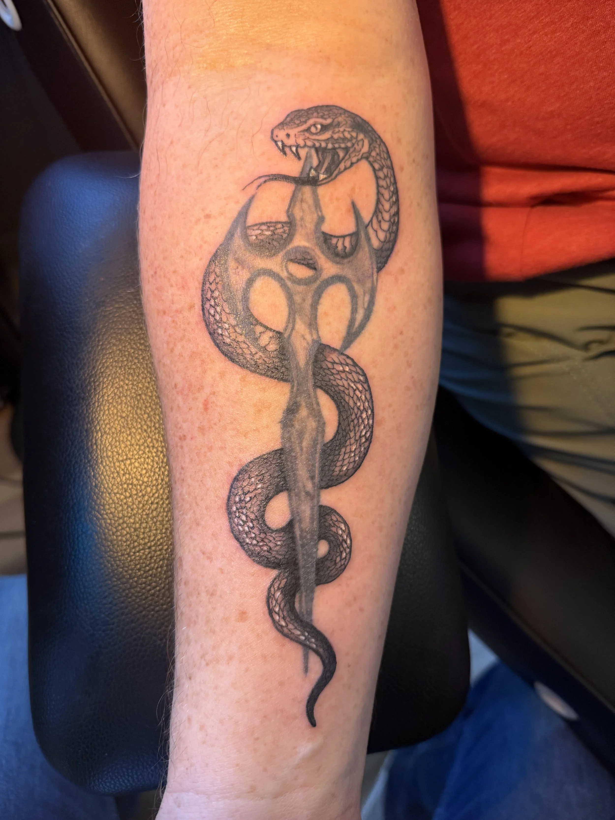 Tattoo of a snake intertwined with a spade symbol on a person's arm.