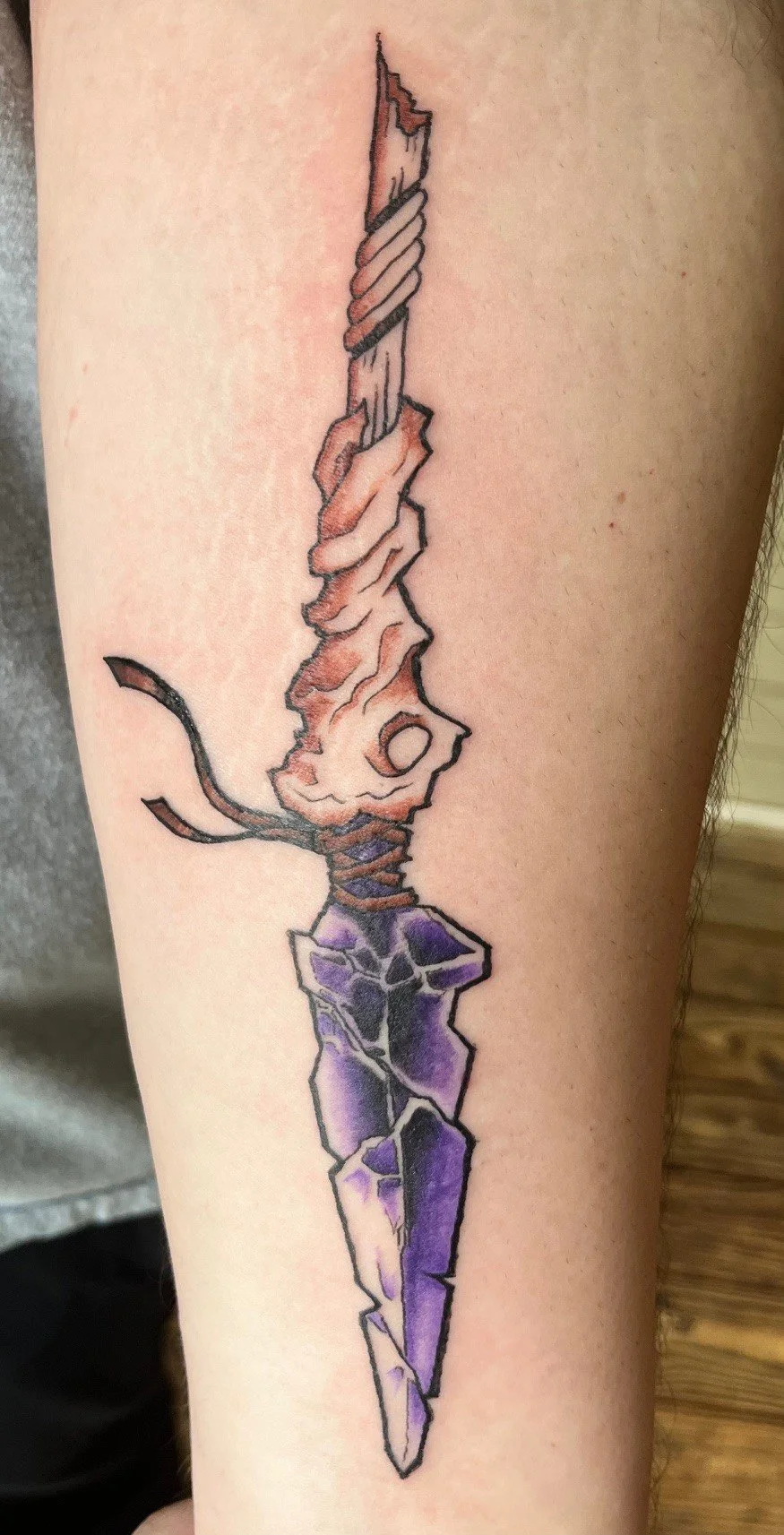 Tattoo of a broken sword with a purple gemstone handle and a twisted, rusted blade.